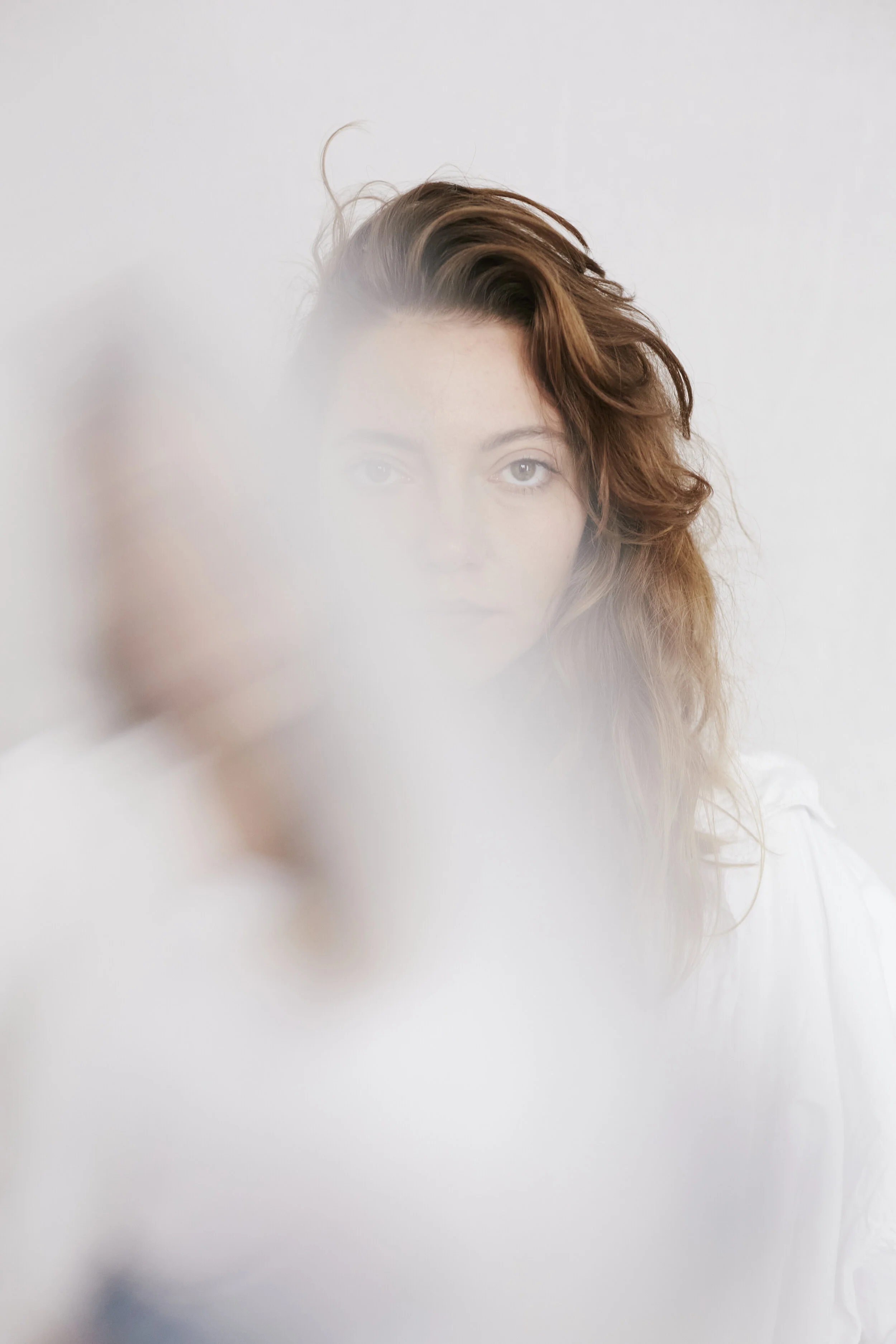 Verschwommenes Porträt einer Frau mit langen Haaren, die teilweise von einem unscharfen, weißen Vordergrund überlagert wird.