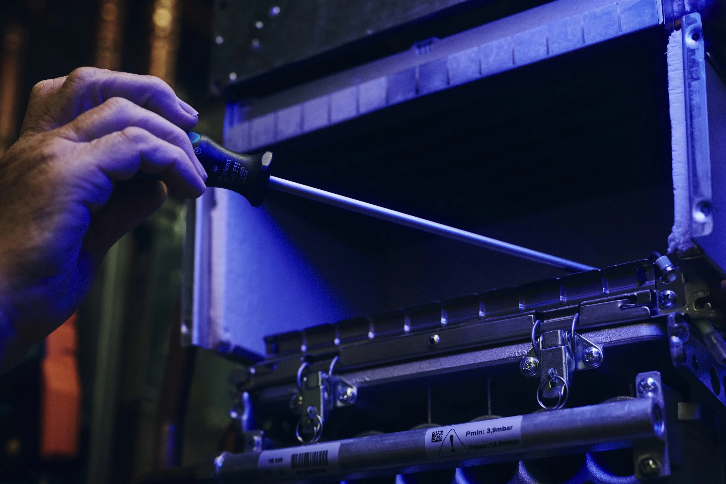Nahaufnahme einer Person, die einen Schraubendreher verwendet, um an einem technischen Gerät zu arbeiten. Der Raum ist in bläulichem Licht beleuchtet.
