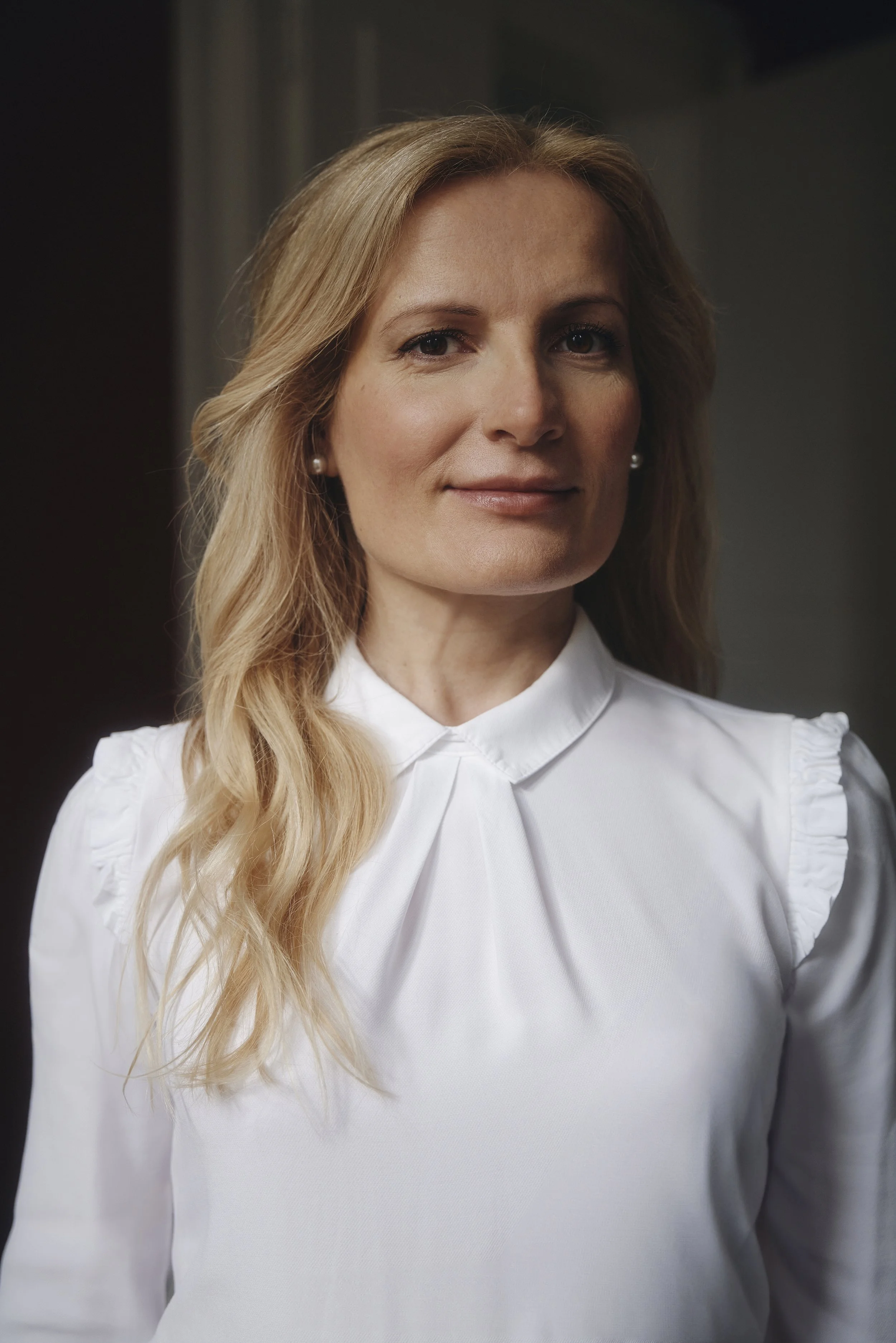 Porträt einer Frau mit langen blonden Haaren in weißer Bluse.