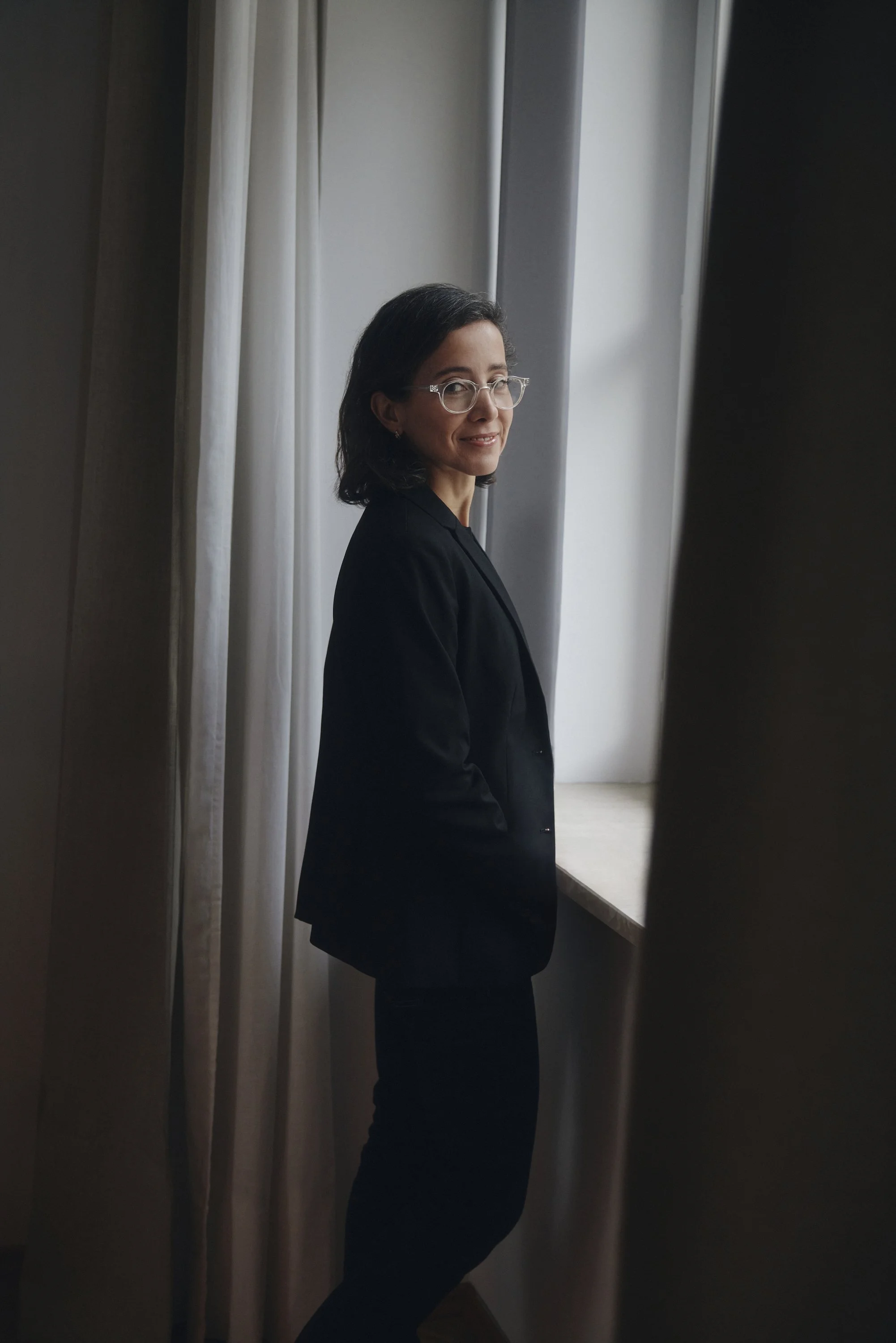 Eine Person in schwarzem Anzug steht an einem Fenster und schaut zur Seite.