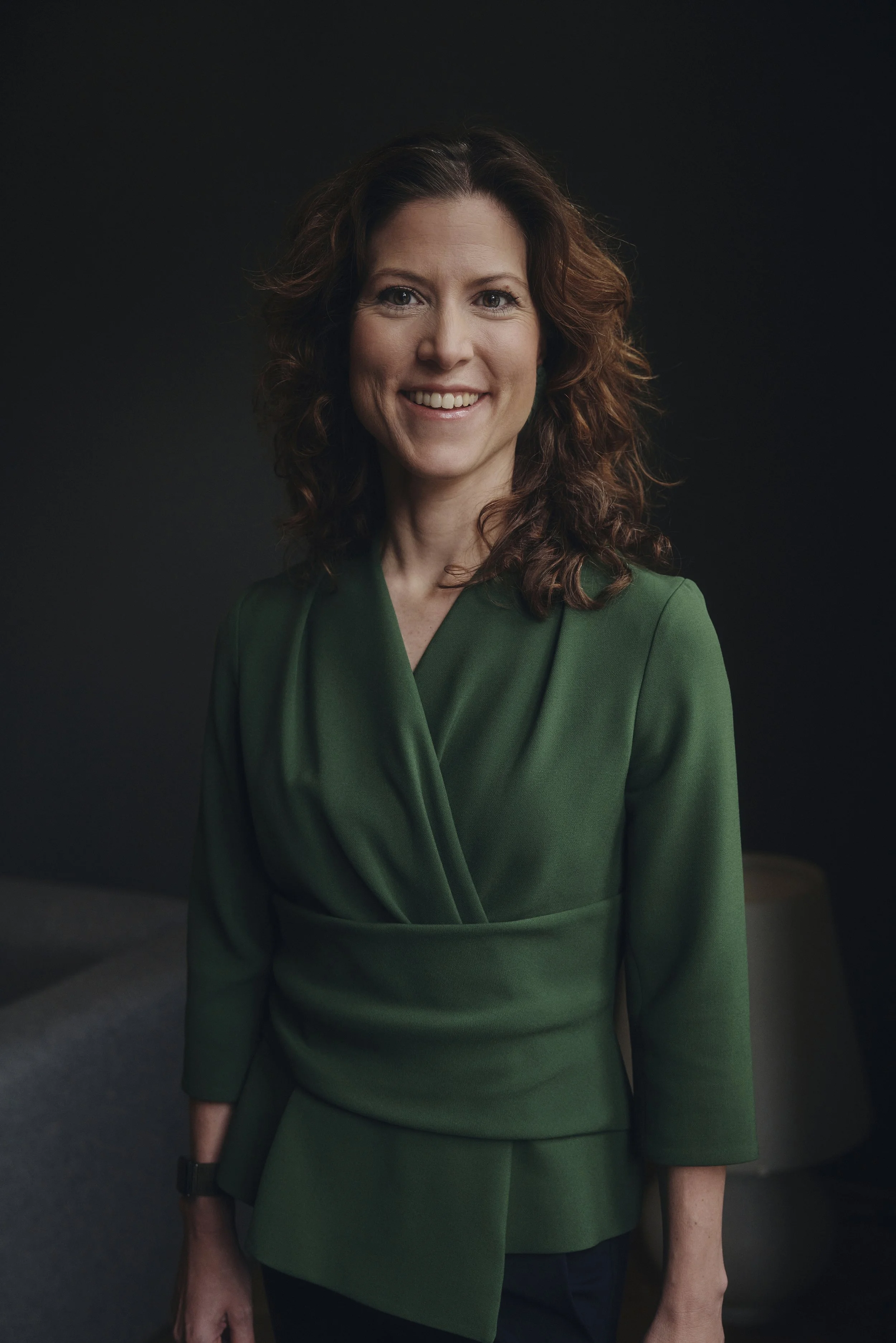 Frau in grüner Bluse vor dunklem Hintergrund lächelt in die Kamera.