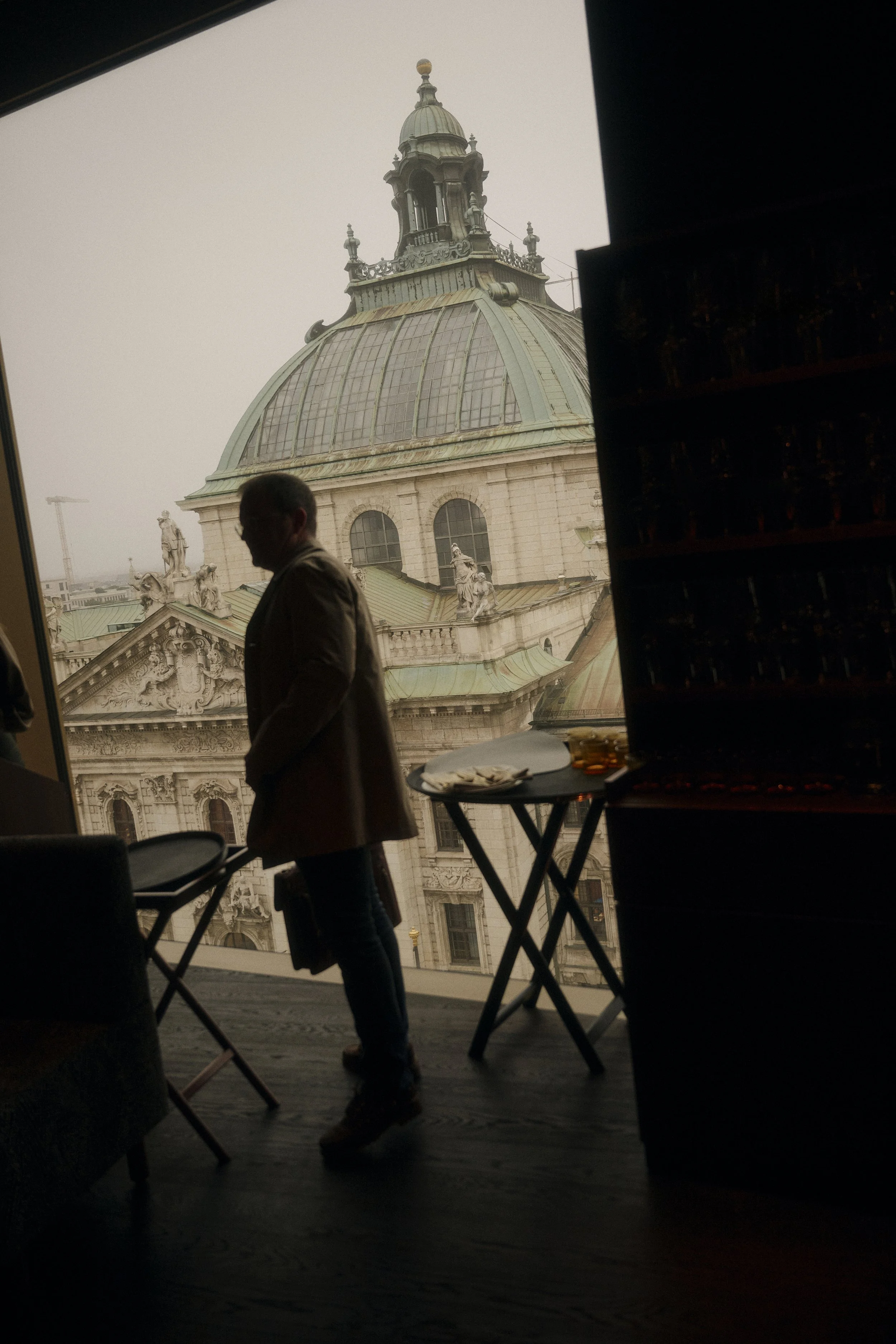 Silhouette eines Mannes in einem Innenraum mit Blick auf ein historisches Gebäude mit Kuppel und Skulpturen im Hintergrund.