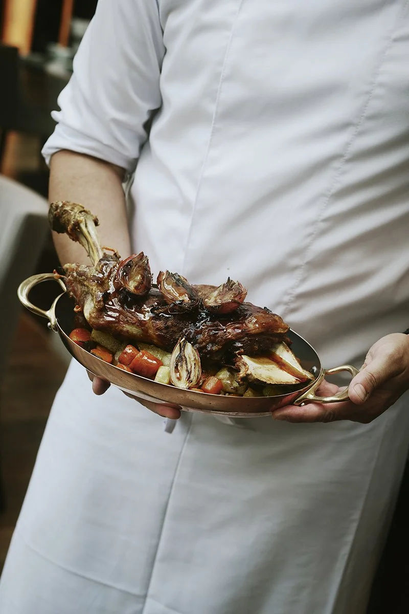 Koch hält eine Kupferpfanne mit gebratenem Lammfleisch und Gemüse.