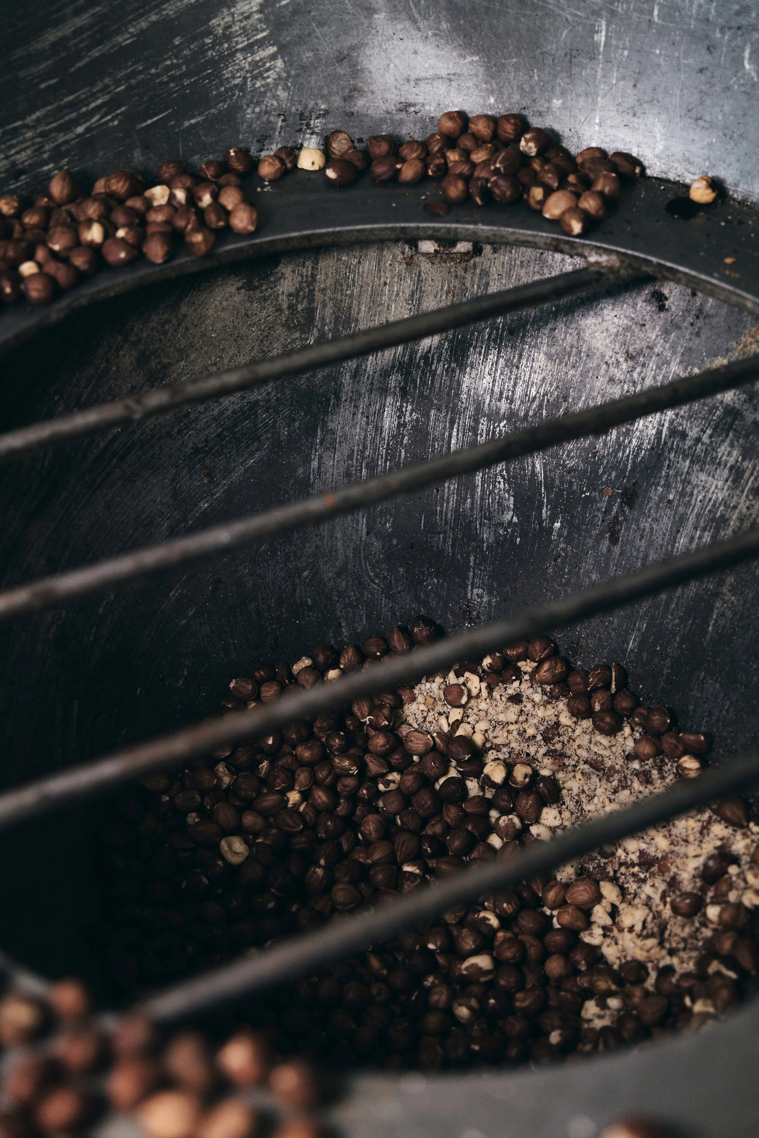 Geröstete Kaffeebohnen und gemahlener Kaffee in einem Metallbehälter mit Gitterstäben.