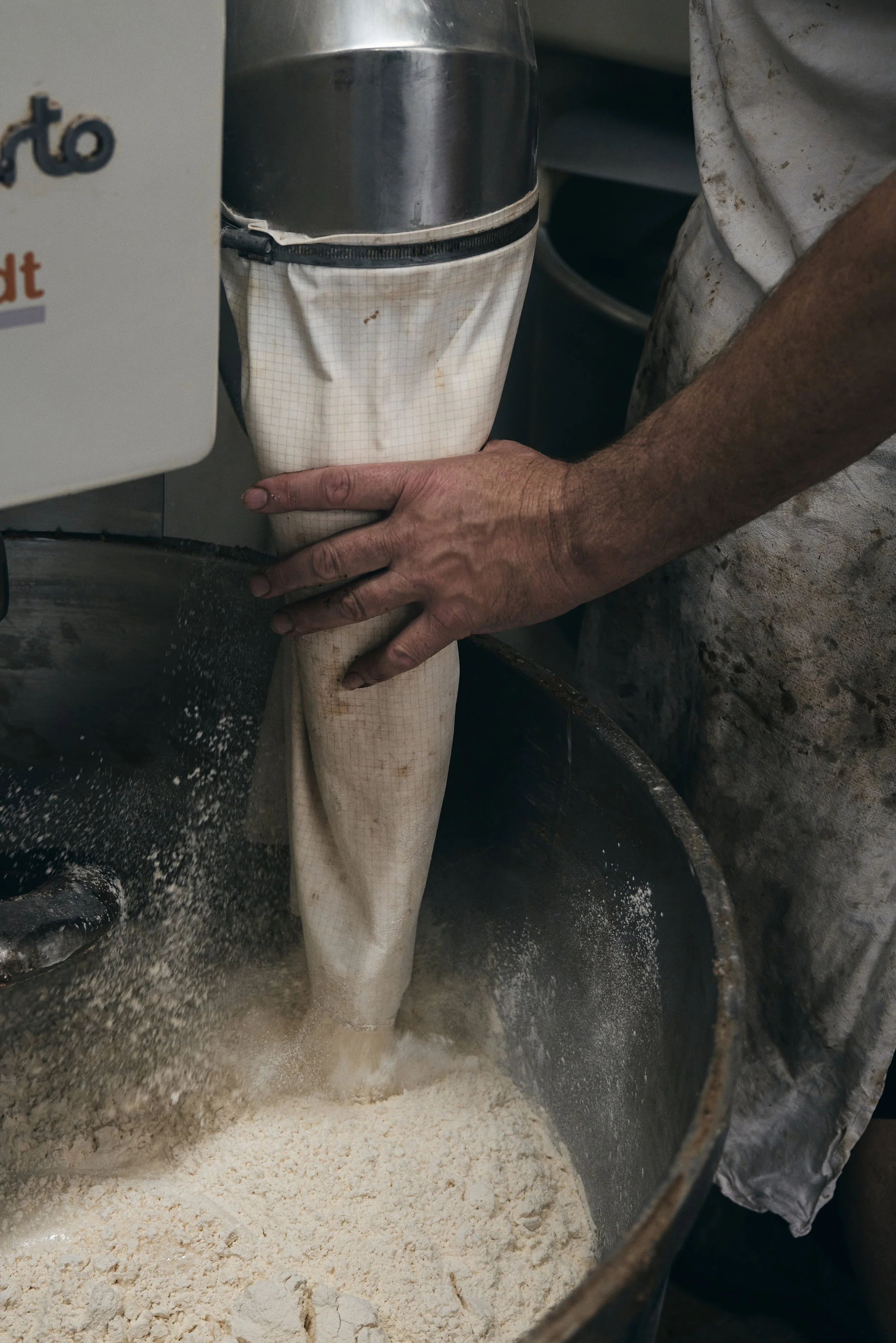 Menschliche Hand hält Stoffrohr, das in großen Behälter mit Mehl führt.