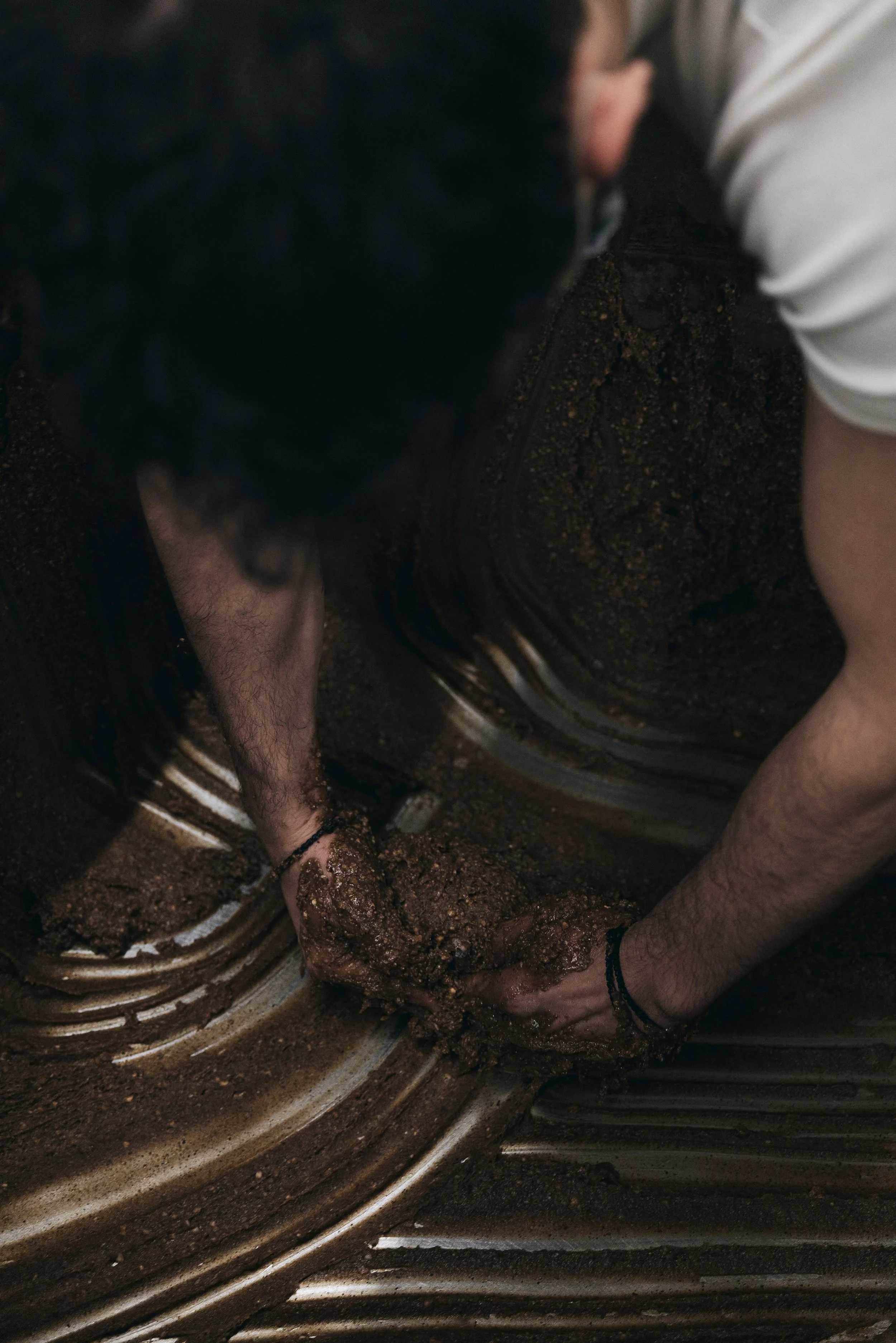 Eine Person knetet dunklen Teig oder Masse mit den Händen.
