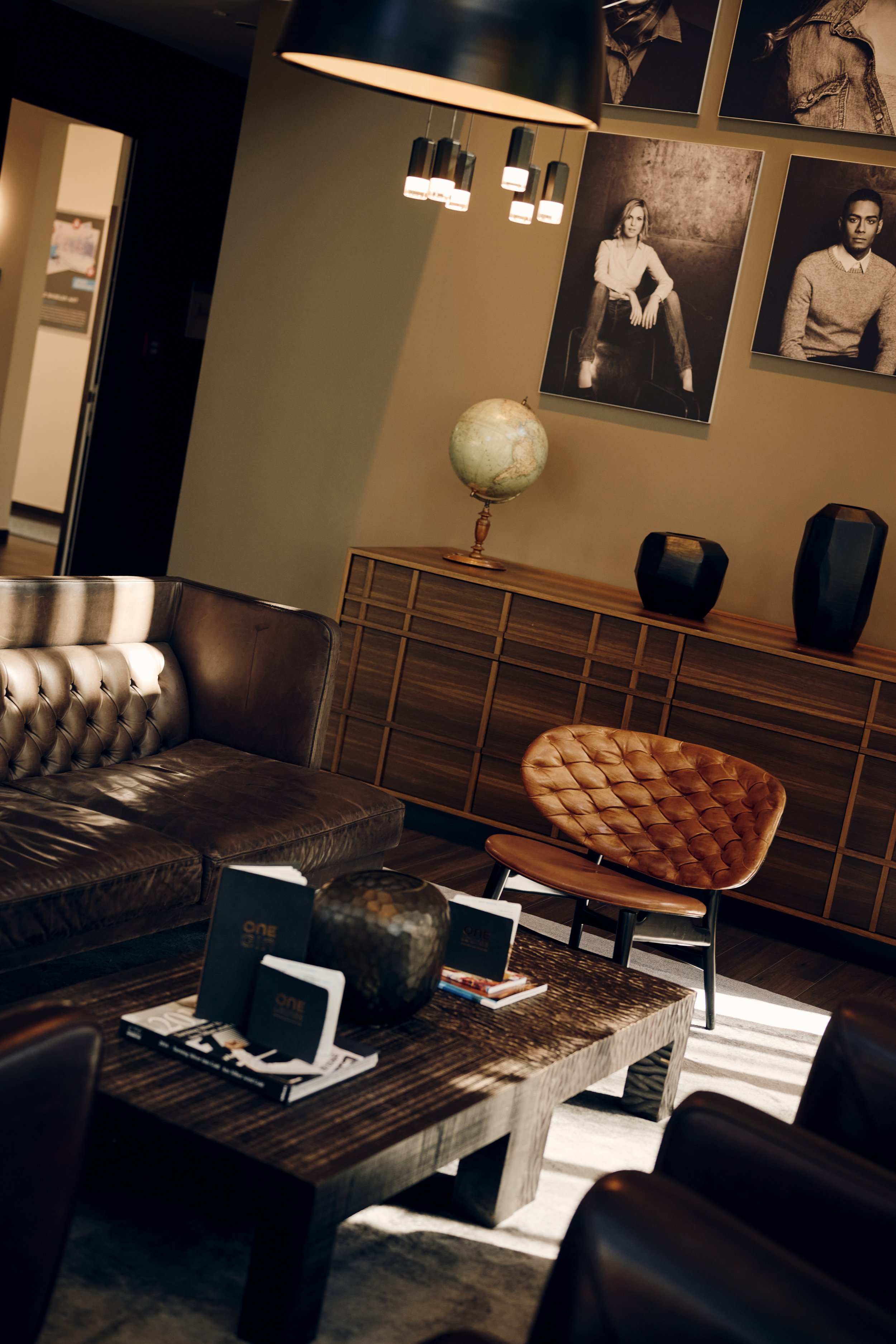 Gemütlicher Wohnbereich mit Ledersofas, Holztisch, Globus, Schwarz-Weiß-Fotografien an der Wand und moderner Beleuchtung.