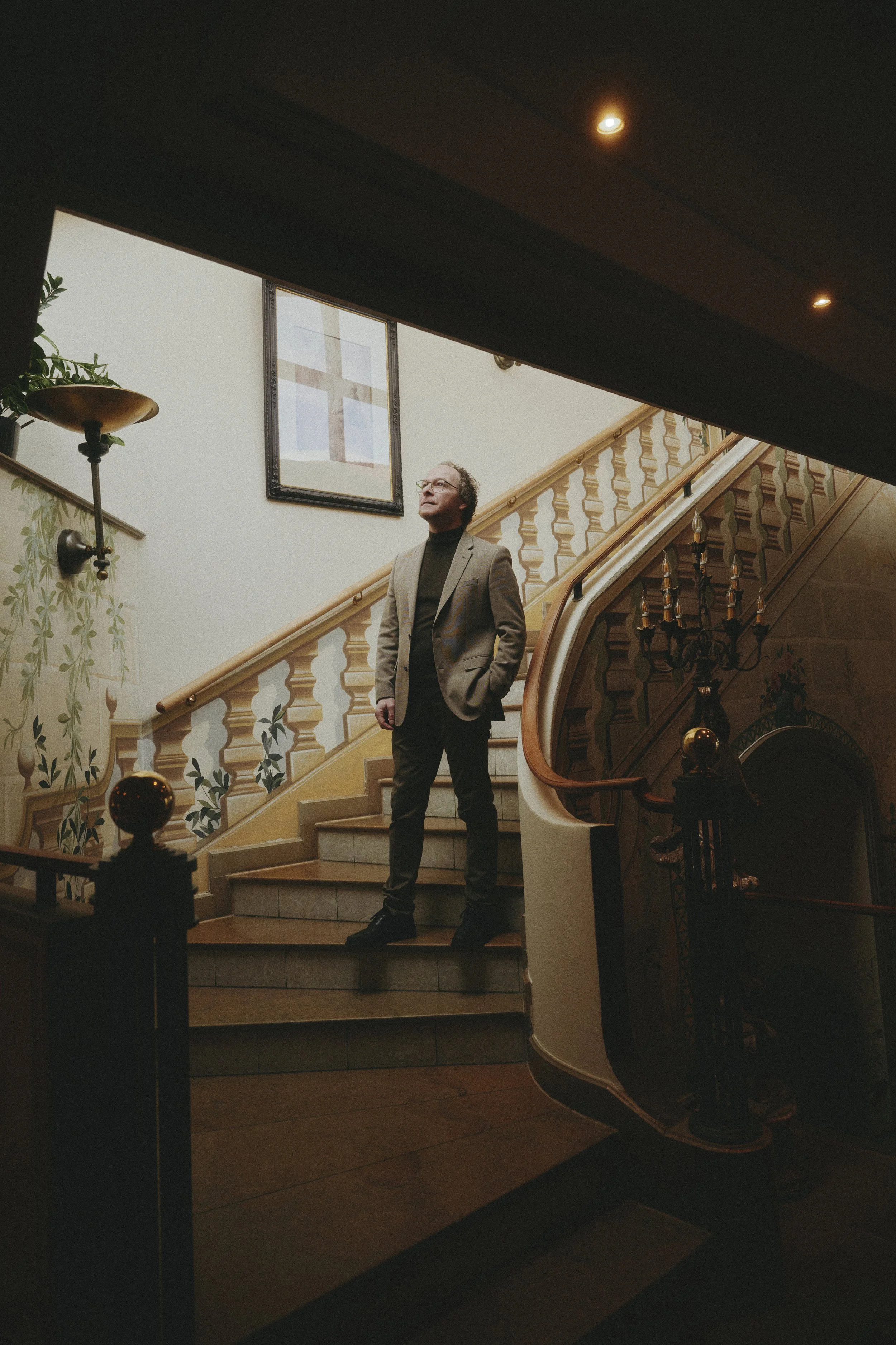 Mann steht auf einer Treppe in einem Gebäude mit Holztäfelung und Wanddekorationen, beleuchtet von oben.