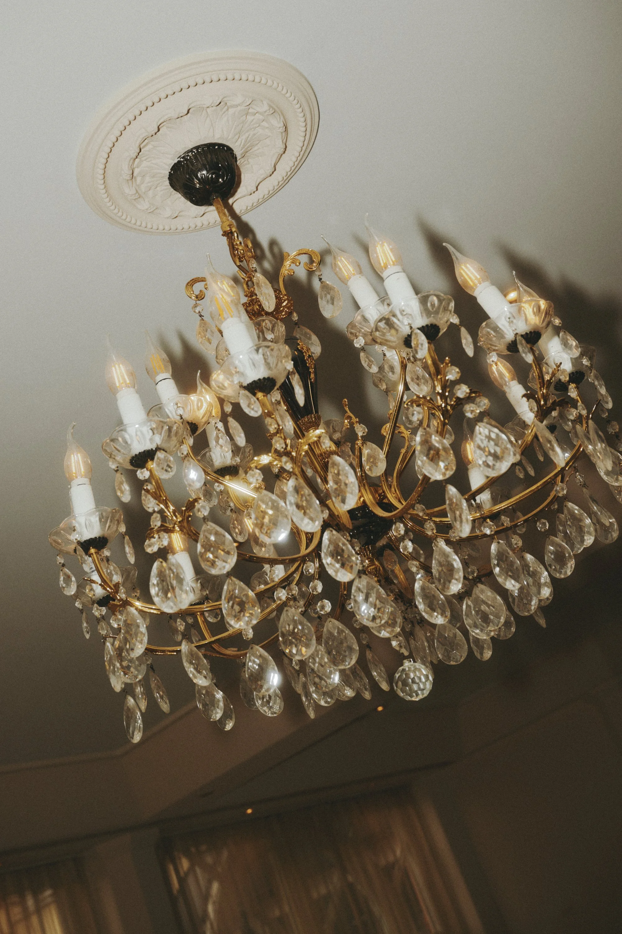 Kronleuchter mit Kristallanhängern und dekorativen Kerzenbirnen, an weißer Decke montiert.