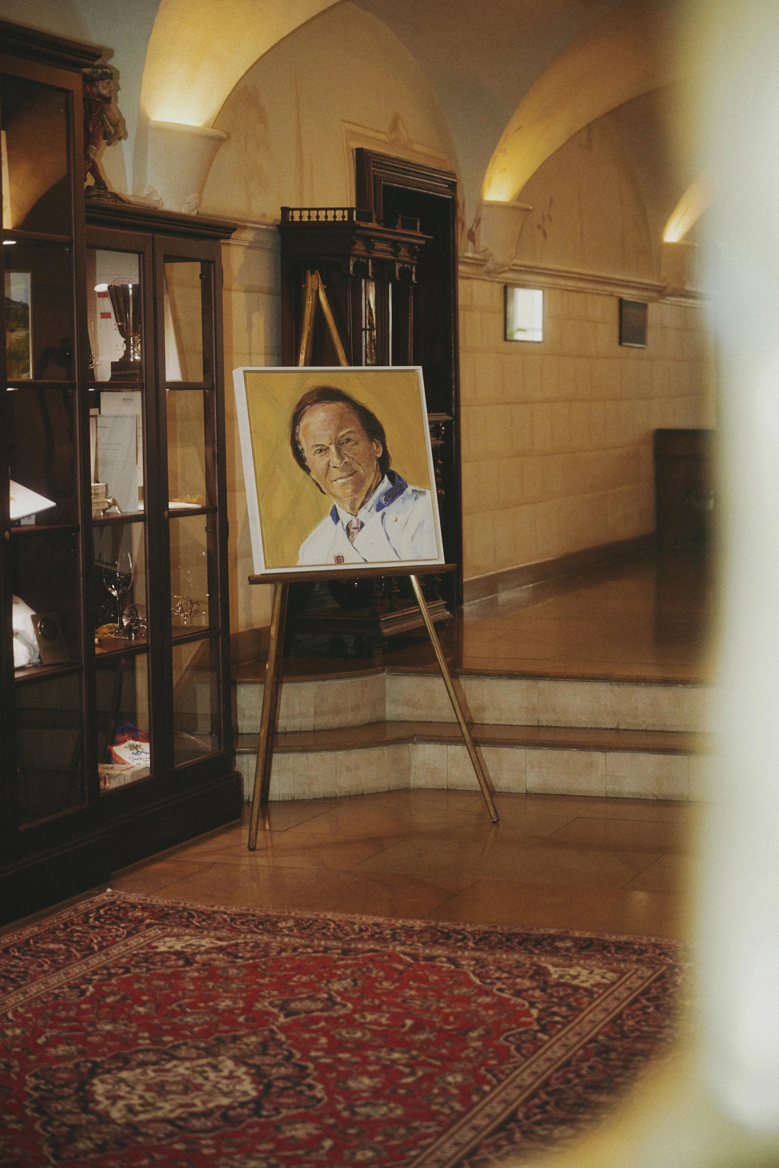 Ein gerahmtes Porträt auf einer Staffelei in einem Raum mit orientalischem Teppich und antiken Möbeln.