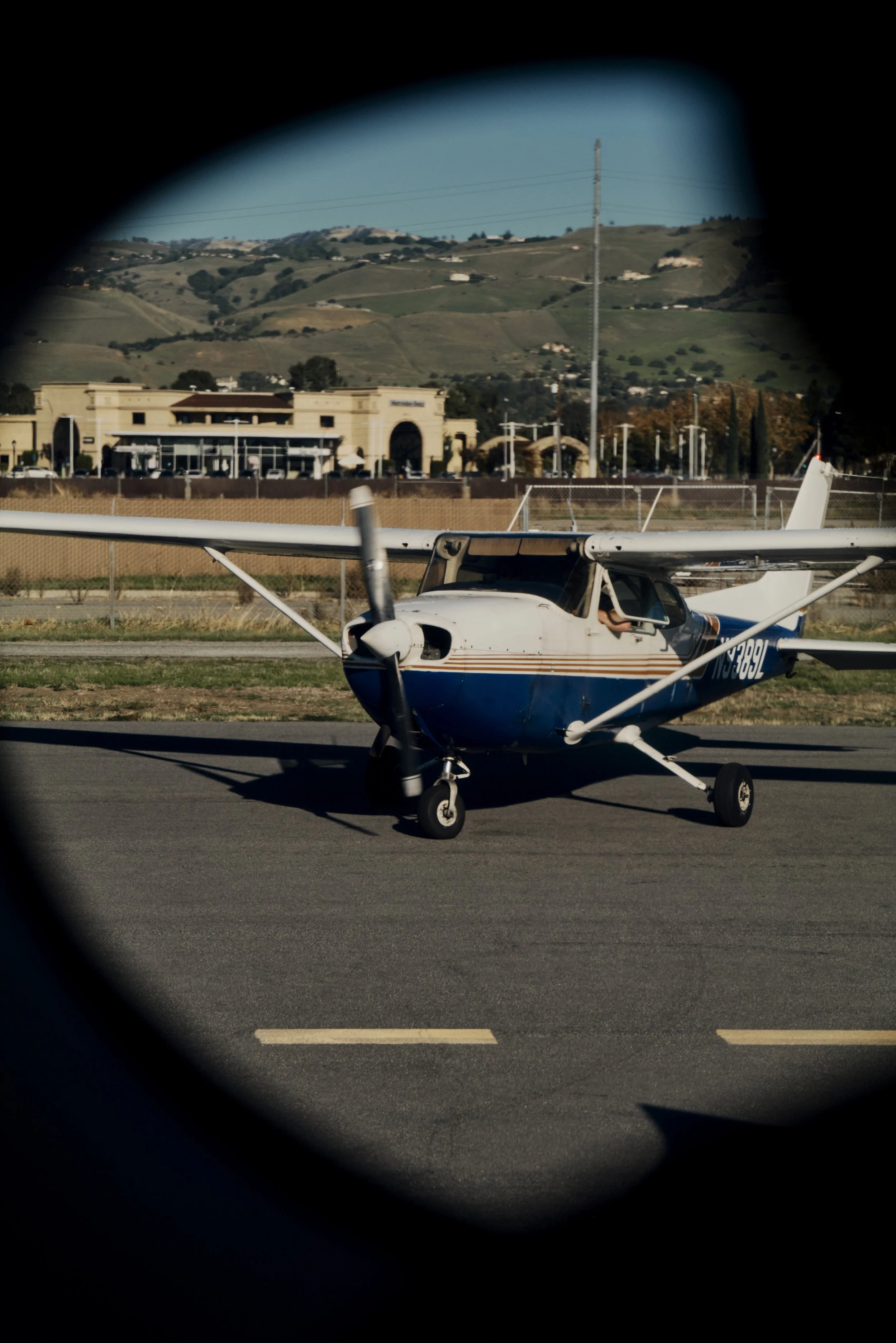 Kleinflugzeug auf Rollbahn eines Flughafens, umgeben von grünen Hügeln und Gebäuden im Hintergrund.
