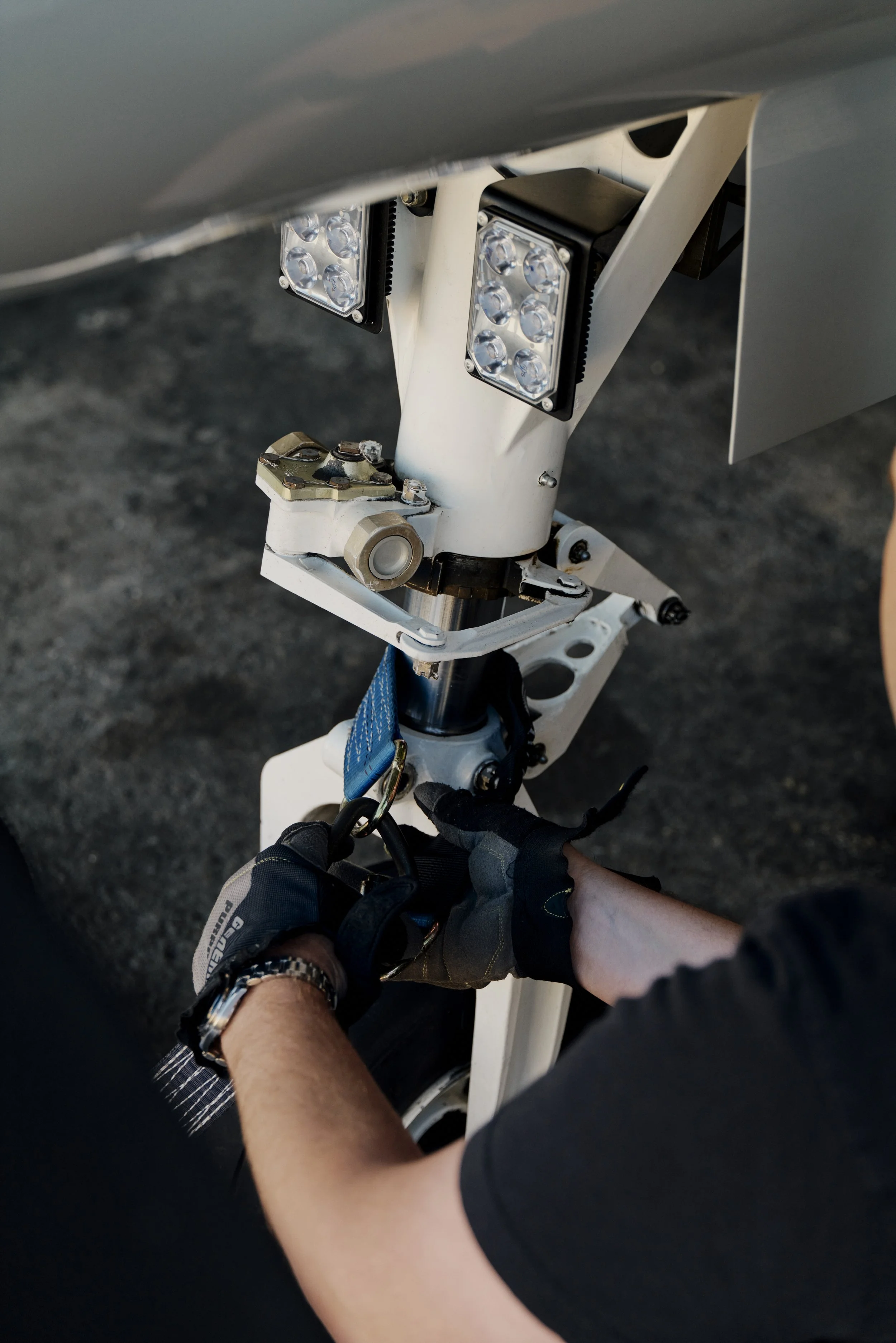 Nahaufnahme eines Flugzeugfahrwerks mit einer Person, die an einem Sicherheitsgurt arbeitet, und LED-Leuchten zu sehen.
