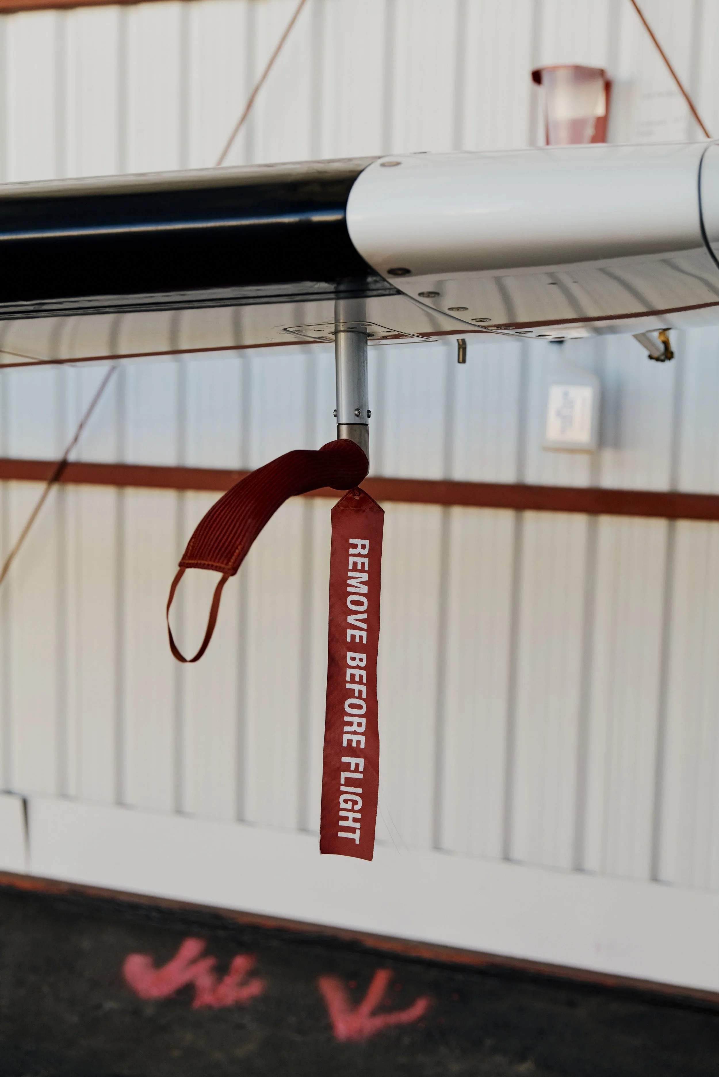 Nahaufnahme eines Flugzeugflügels mit einem roten Sicherheitsband, auf dem „REMOVE BEFORE FLIGHT“ steht.
