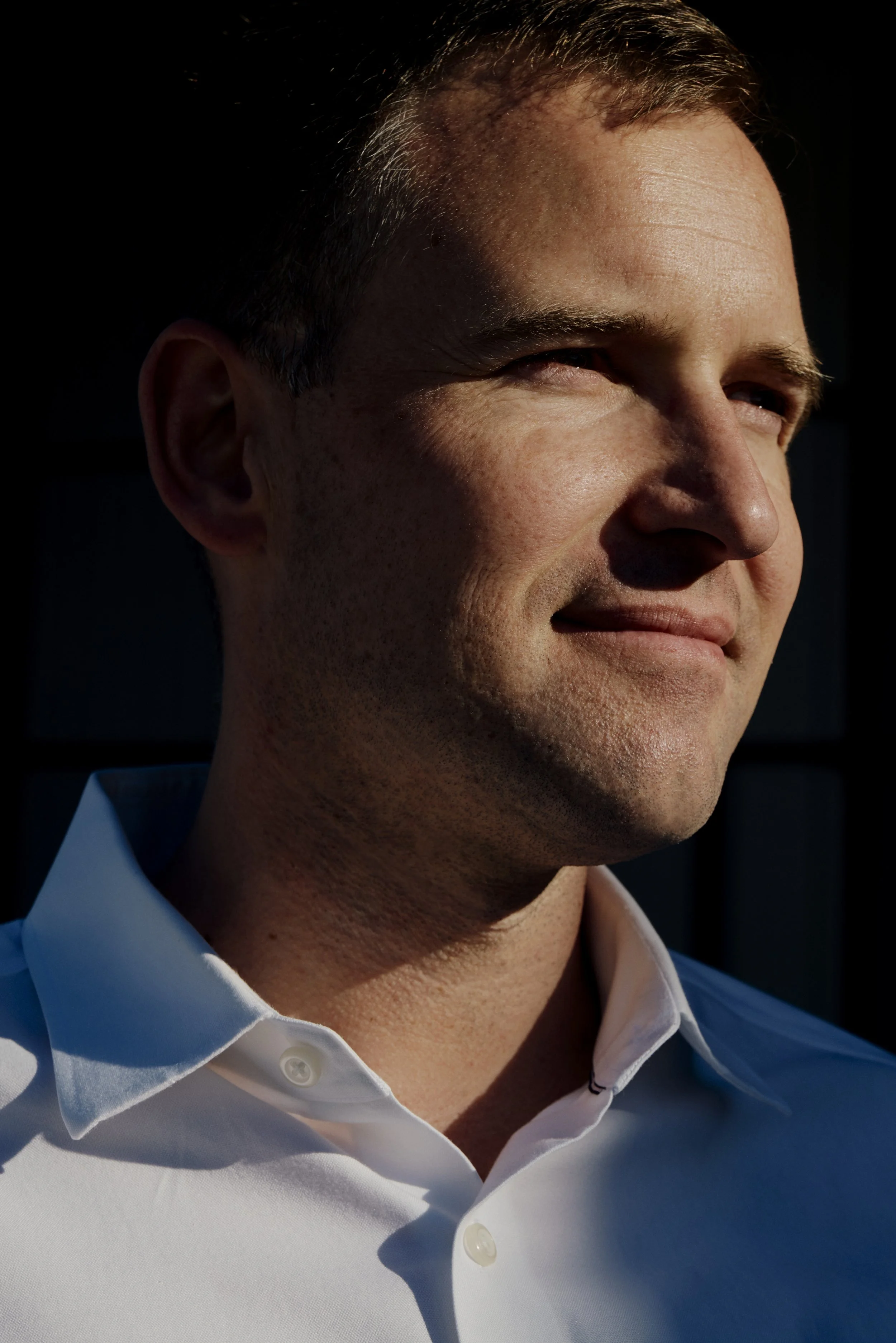 Nahaufnahme einer lächelnden Person im Sonnenschein, die zur Seite schaut, in einem weißen Hemd.