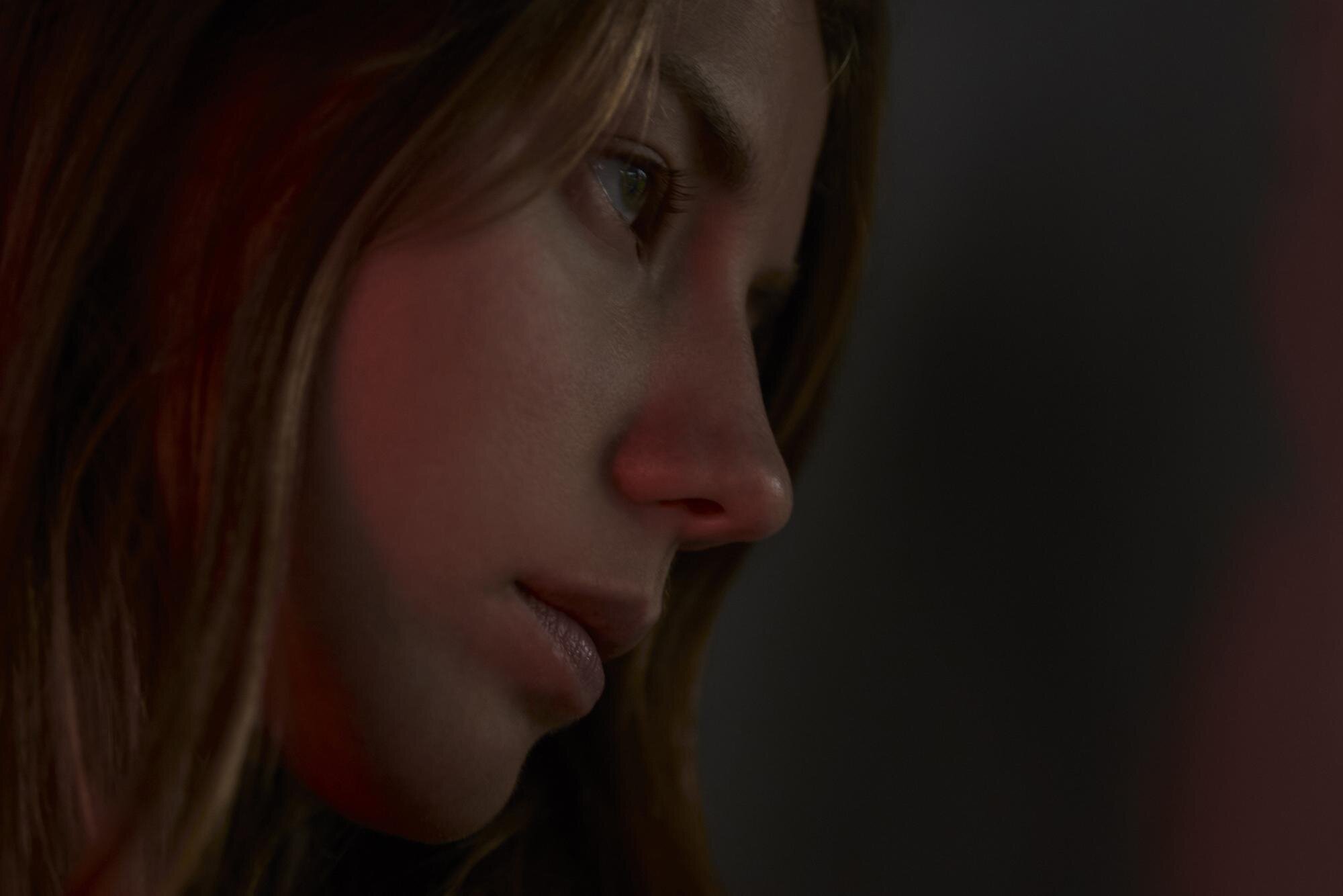 Nahaufnahme eines nachdenklichen Gesichts mit langen Haaren und einem fokussierten Blick, beleuchtet von sanftem Licht.