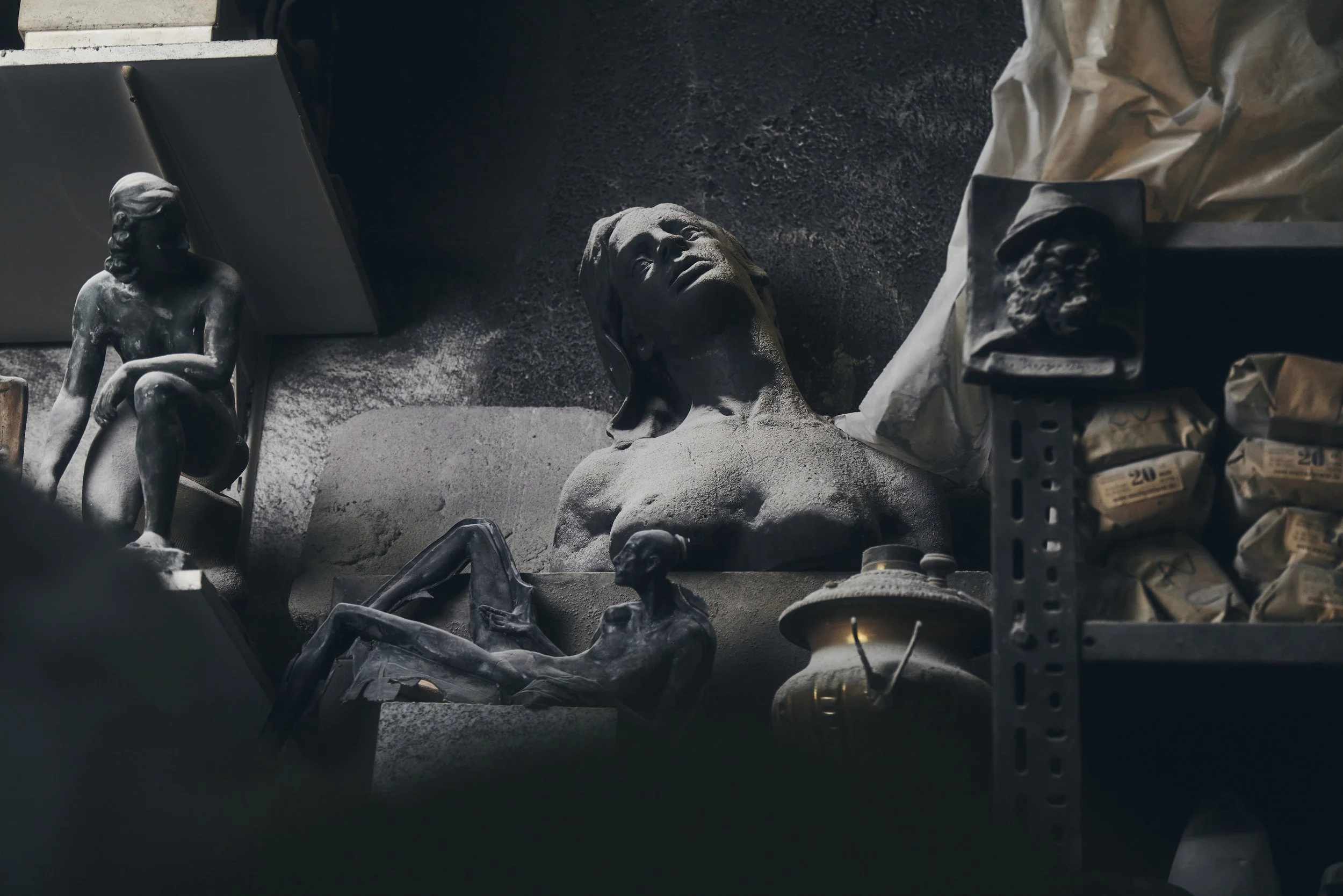 Statuen und Skulpturen in einem dunklen Raum; Staub und Lagerregale sichtbar.