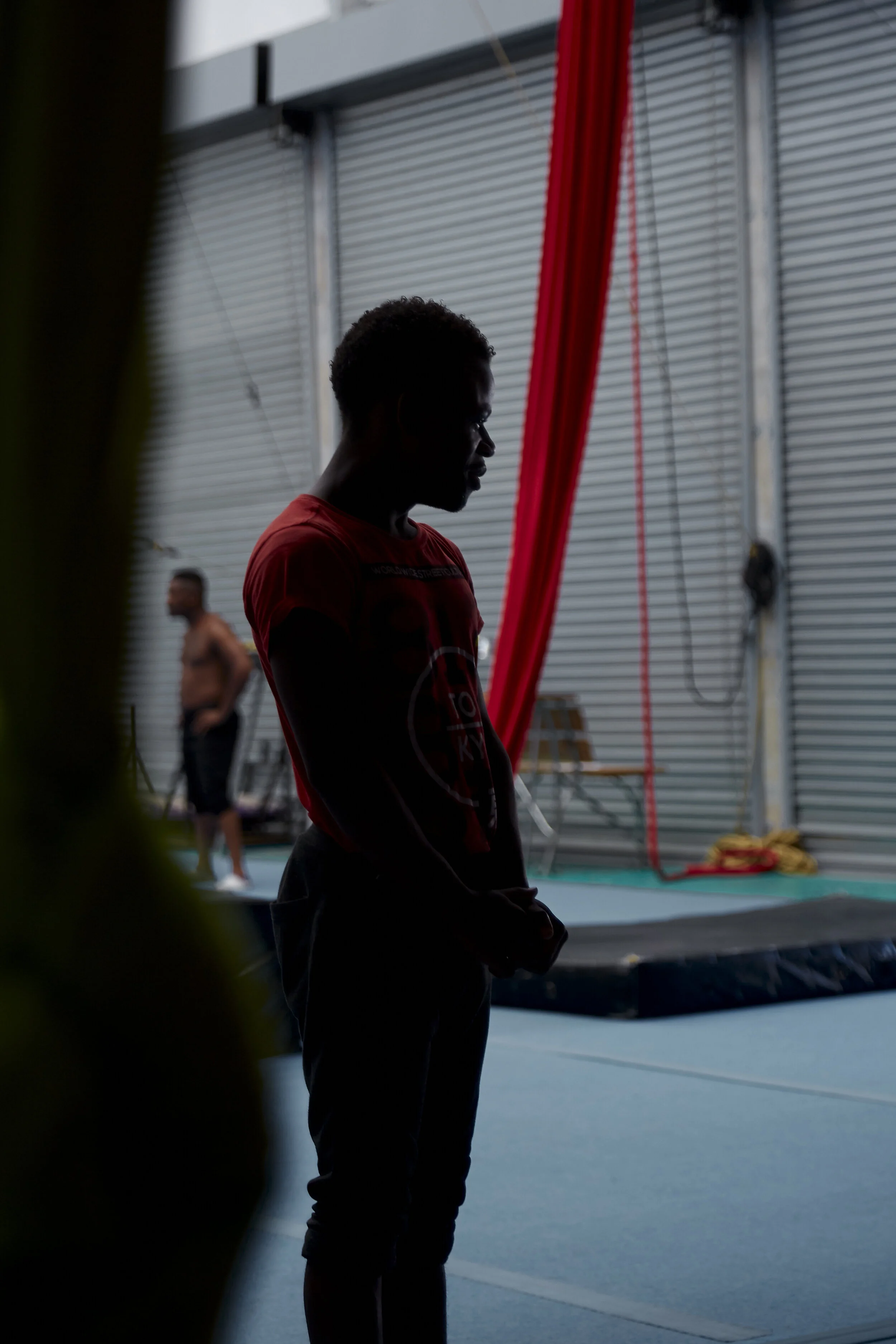 Schattenriss eines Mannes in einem Innenraum mit roten Vorhängen und einem geschlossenen Garagentor im Hintergrund.