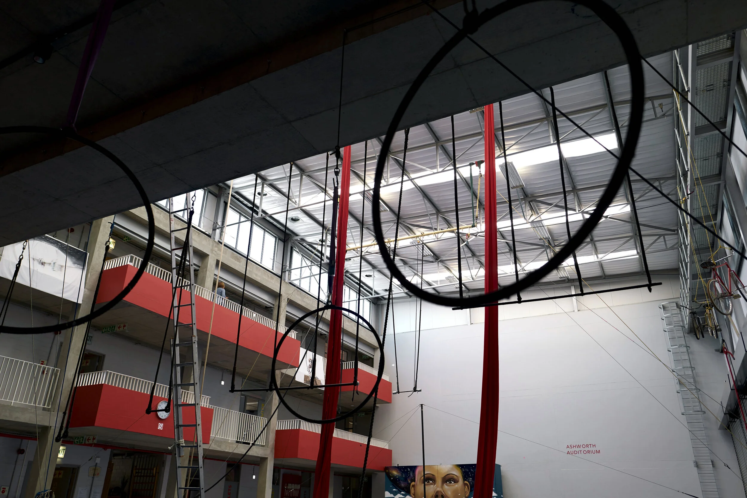 Innenansicht eines Gebäudes mit roten Balkonen und Hängegeräten, wahrscheinlich für Akrobatik, und einer bemalten Wand im Hintergrund.