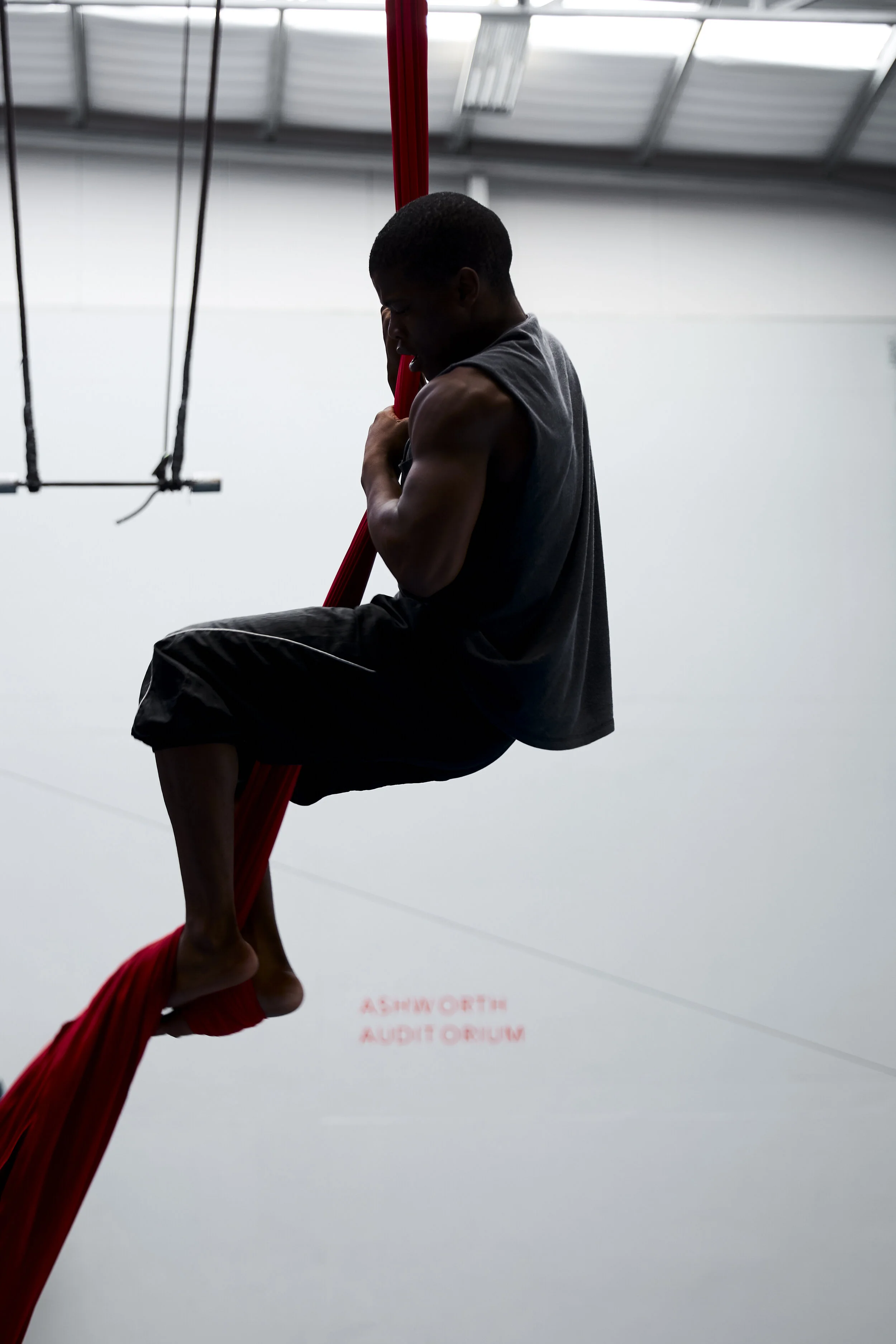 Ein Mann klettert an einem roten, vertikalen Stoff im Ashworth Auditorium.