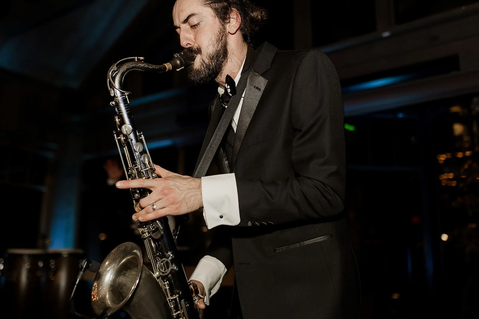 A man in a tuxedo playing the saxophone at an indoor event or performance.