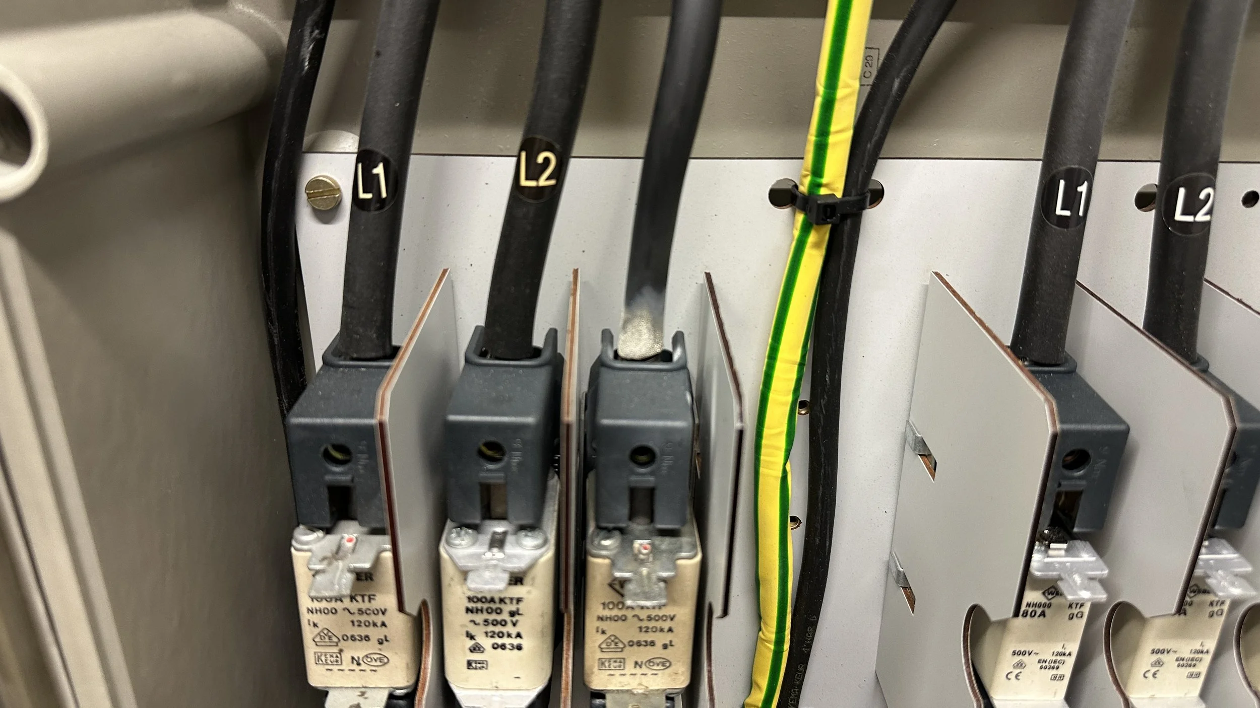 Electrical circuit breaker panel with black wires labeled L1, L2 and L3 wire, and a yellow and green grounding wire. Mespatronen, verdeelinrichting, SVI, meterkast