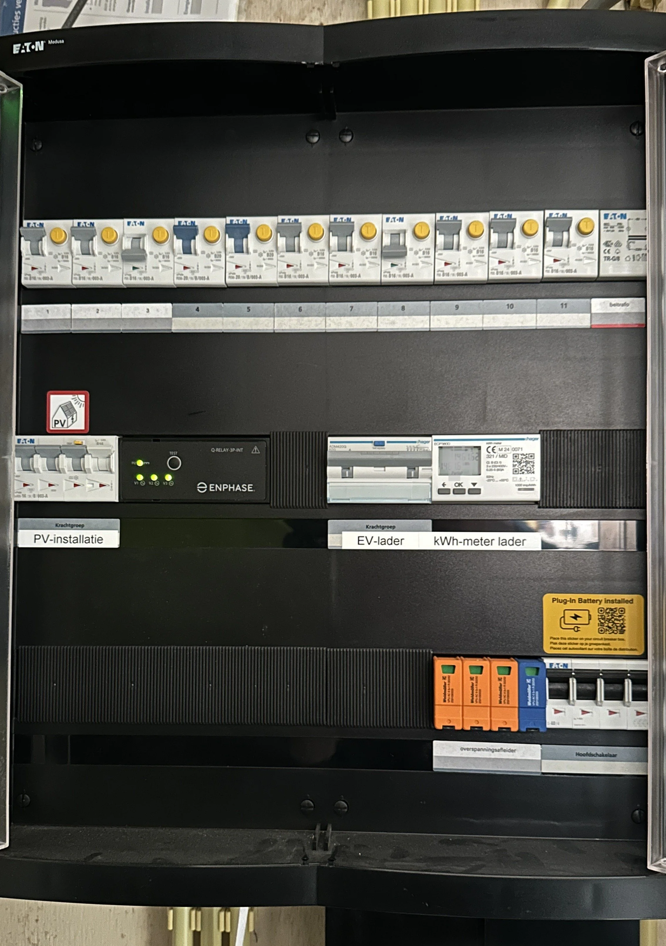 Electrical control panel with circuit breakers, a digital meter, and labels for PV installation and EV charger.