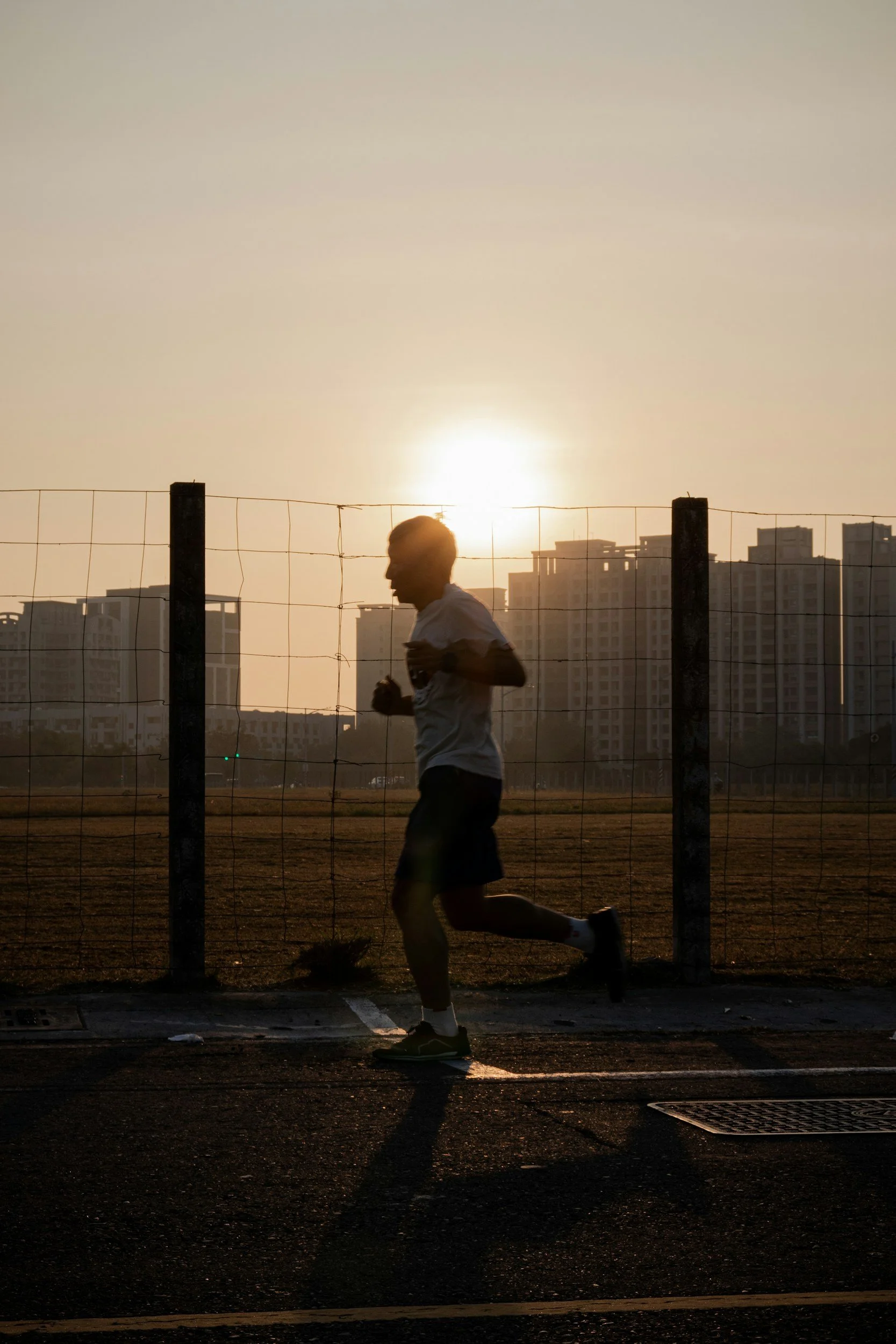 Jogger läuft bei Sonnenuntergang auf einer Sportbahn, im Hintergrund Stadtgebäude sichtbar.