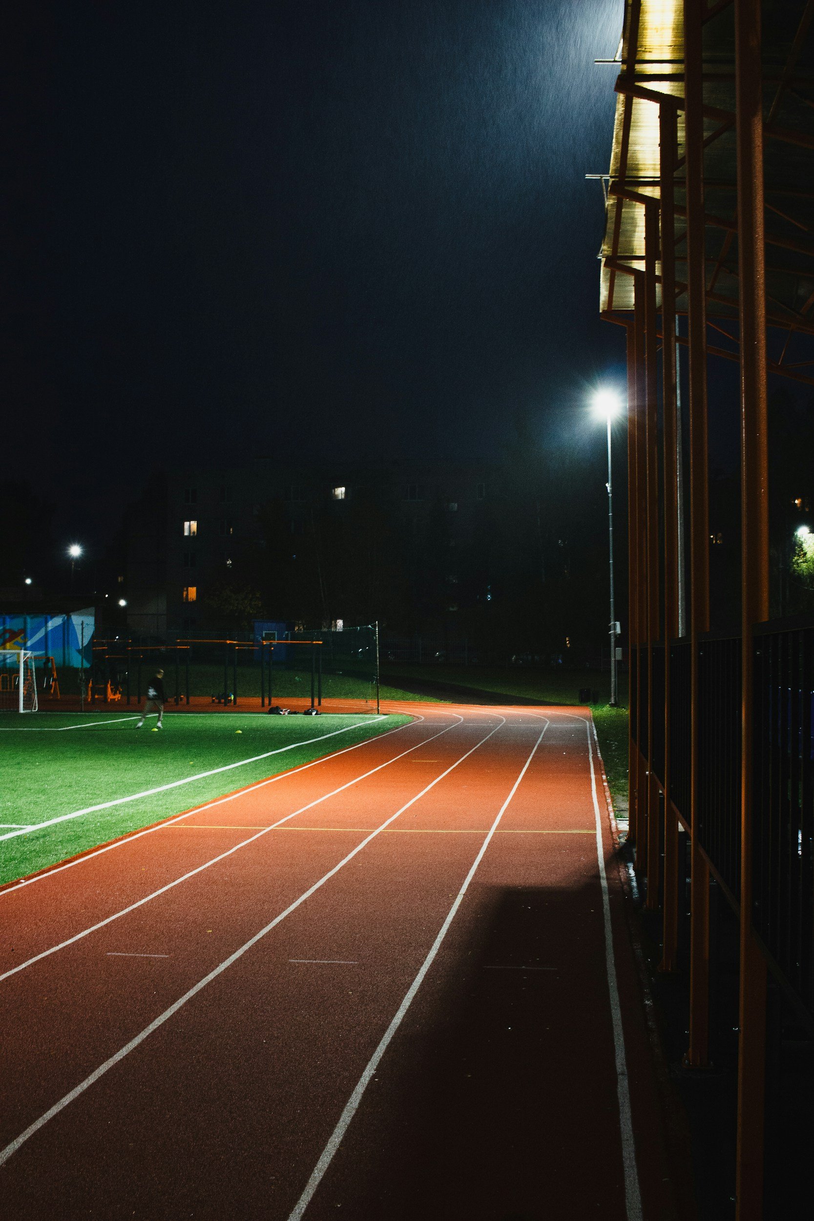 Leerer, beleuchteter Laufbahn bei Nacht mit Sportsfield im Hintergrund.