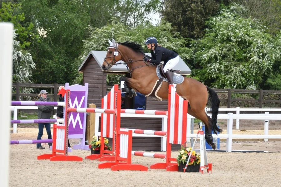 A rider and horse jumping over a colorful obstacle in an outdoor equestrian arena.