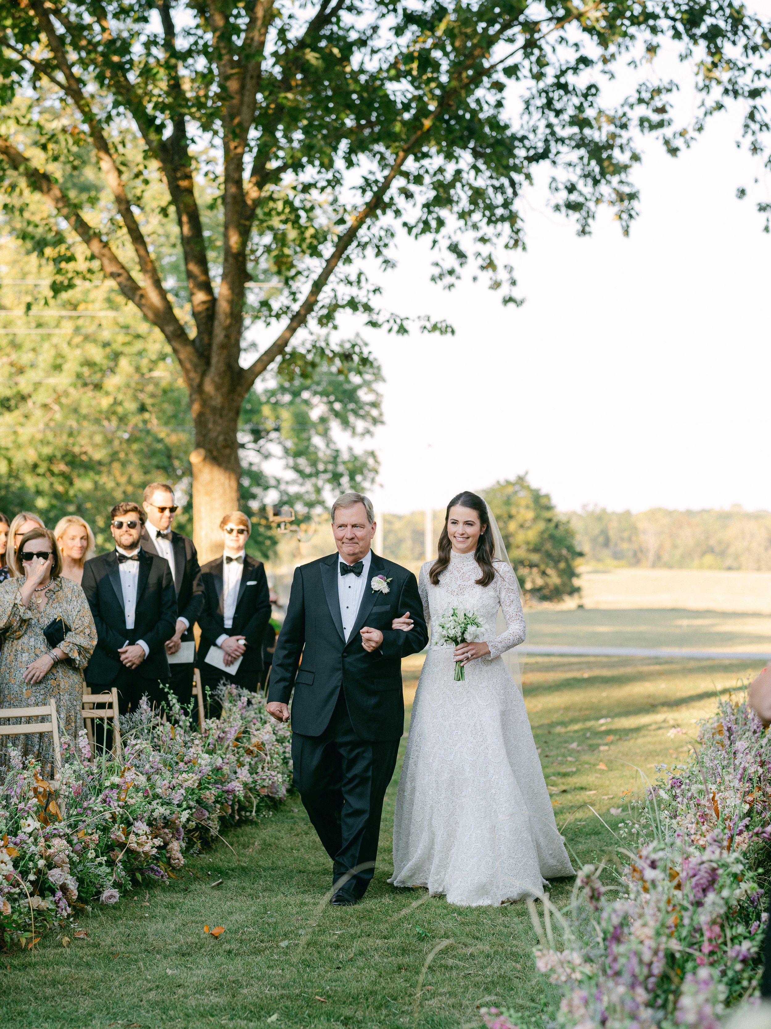 Bride walks down an aisle flanked by floral masterpieces that both accentuate and uplift the environment