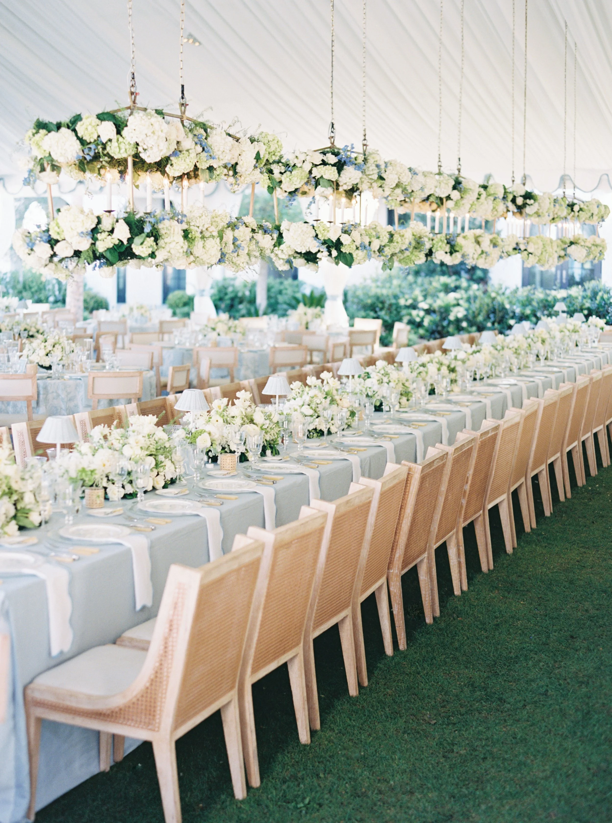 Impressive and luxurious wedding reception on Sea Island features long table, show-stopping hanging floral arrangements and blue hues that accentuate the oceanside party
