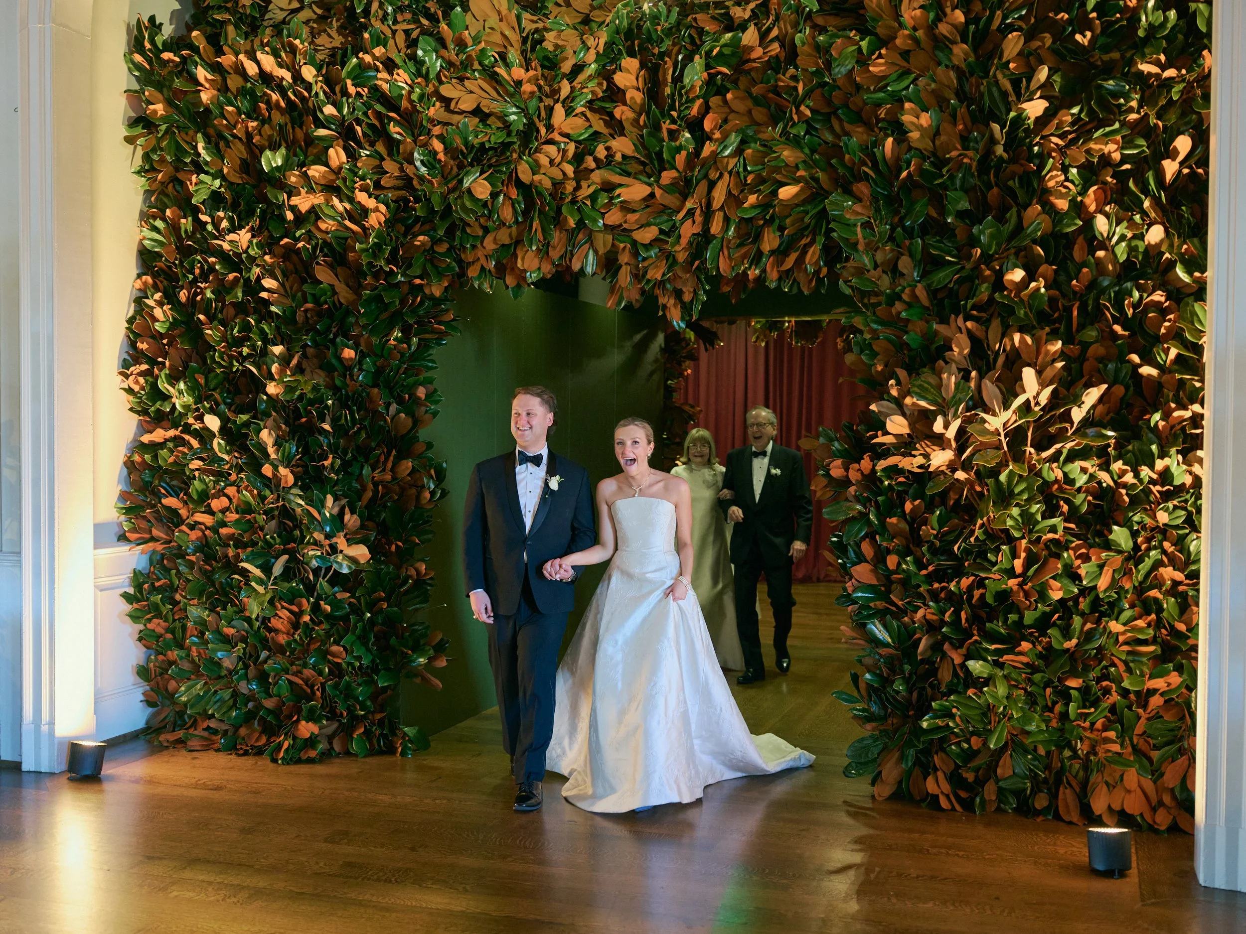 Bride and groom make a grand entrance through an entire wall of magnolia leaves