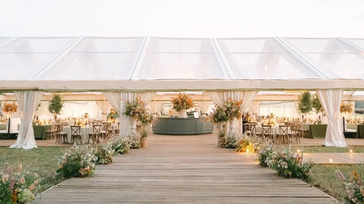Deluxe wedding tent with romantic floral displays lining the walkway and a central bar with a large floral centerpiece