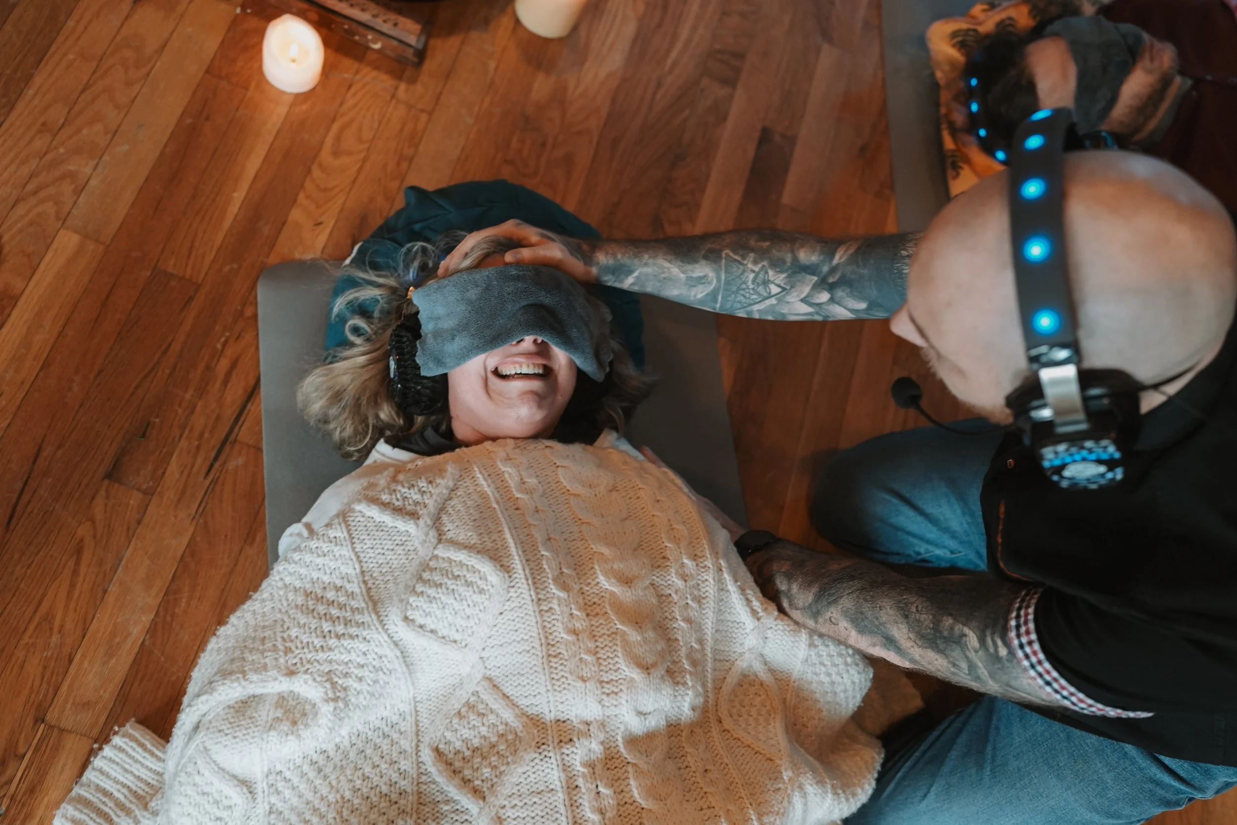 A participant resting during a breathwork session while the facilitator provides attentive, consent-based support in a calm, therapeutic environment.