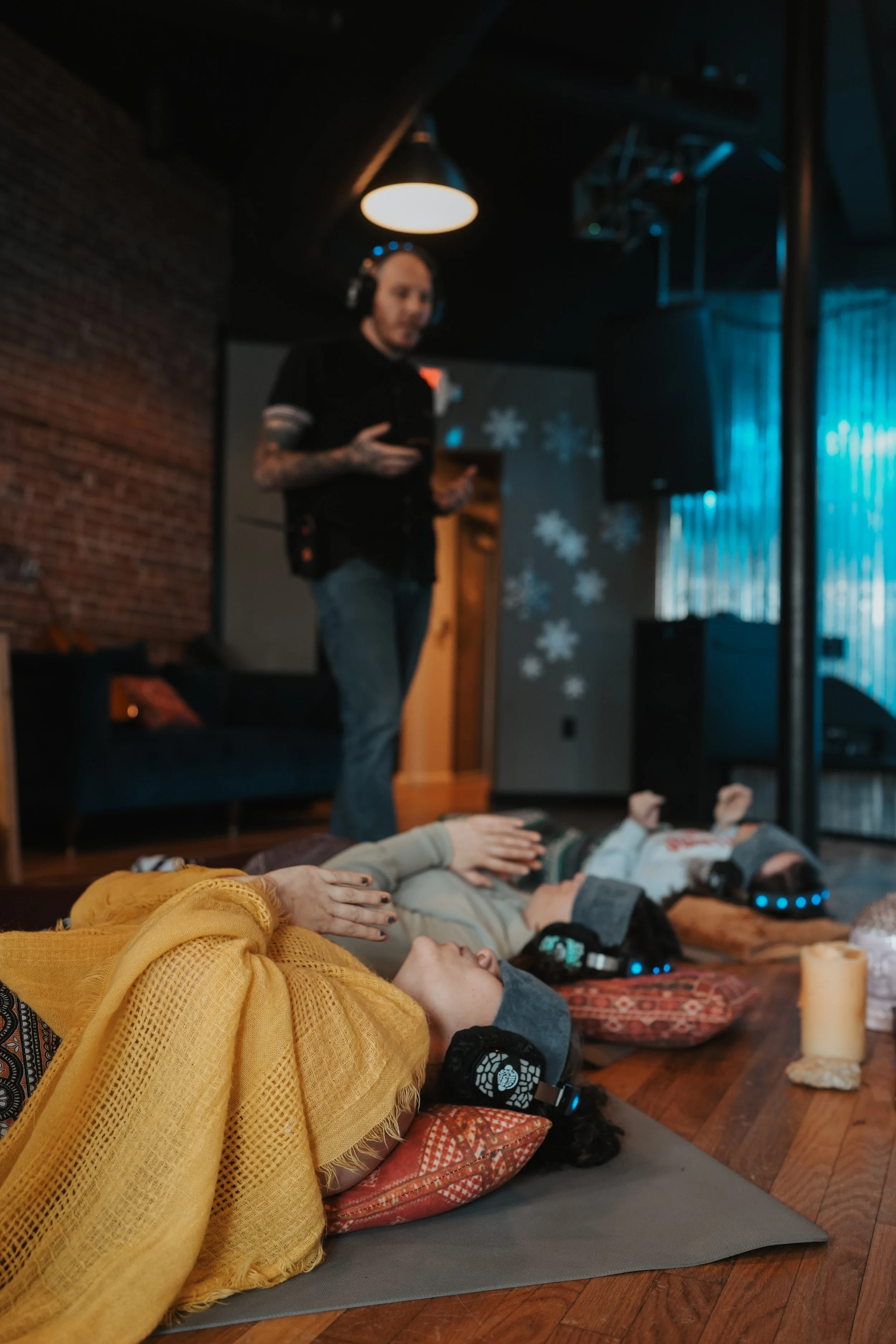 Adults resting comfortably on mats during a guided breathwork session, listening through headphones in a calm, supportive indoor setting designed for relaxation and emotional processing.