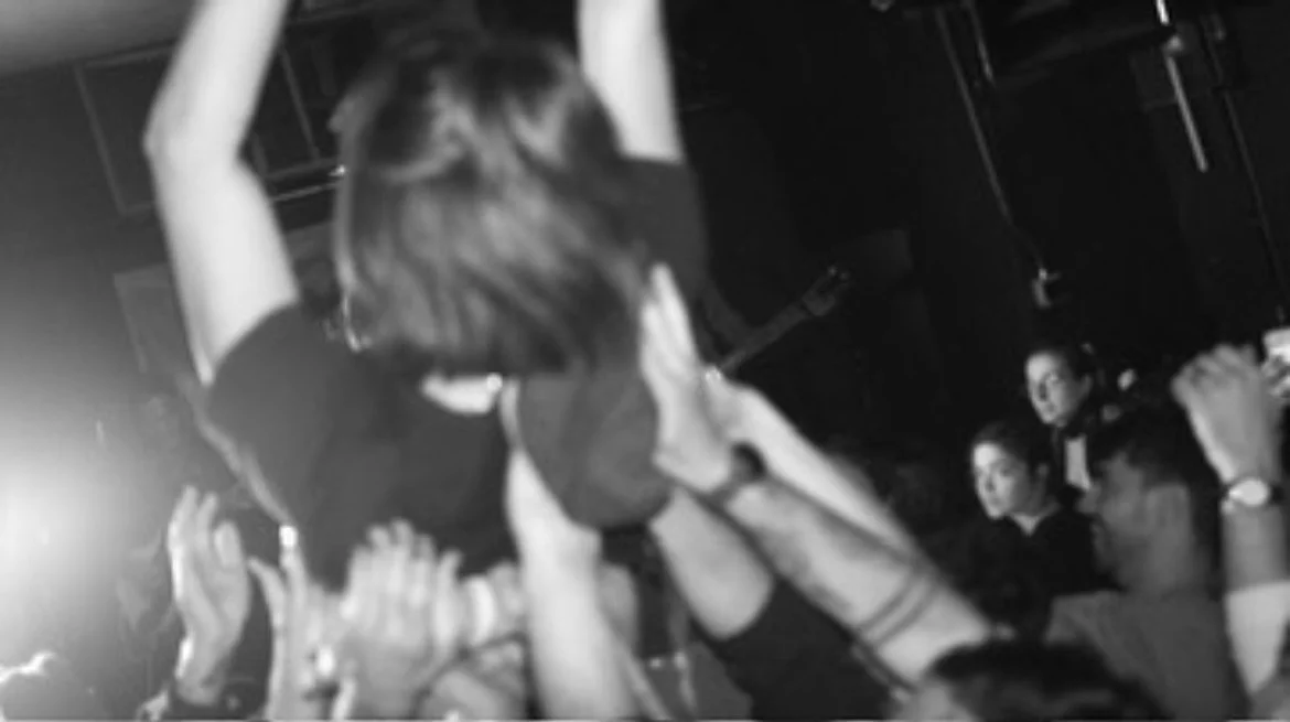 Person crowd surfing at a concert or event with audience members holding up their hands to support.