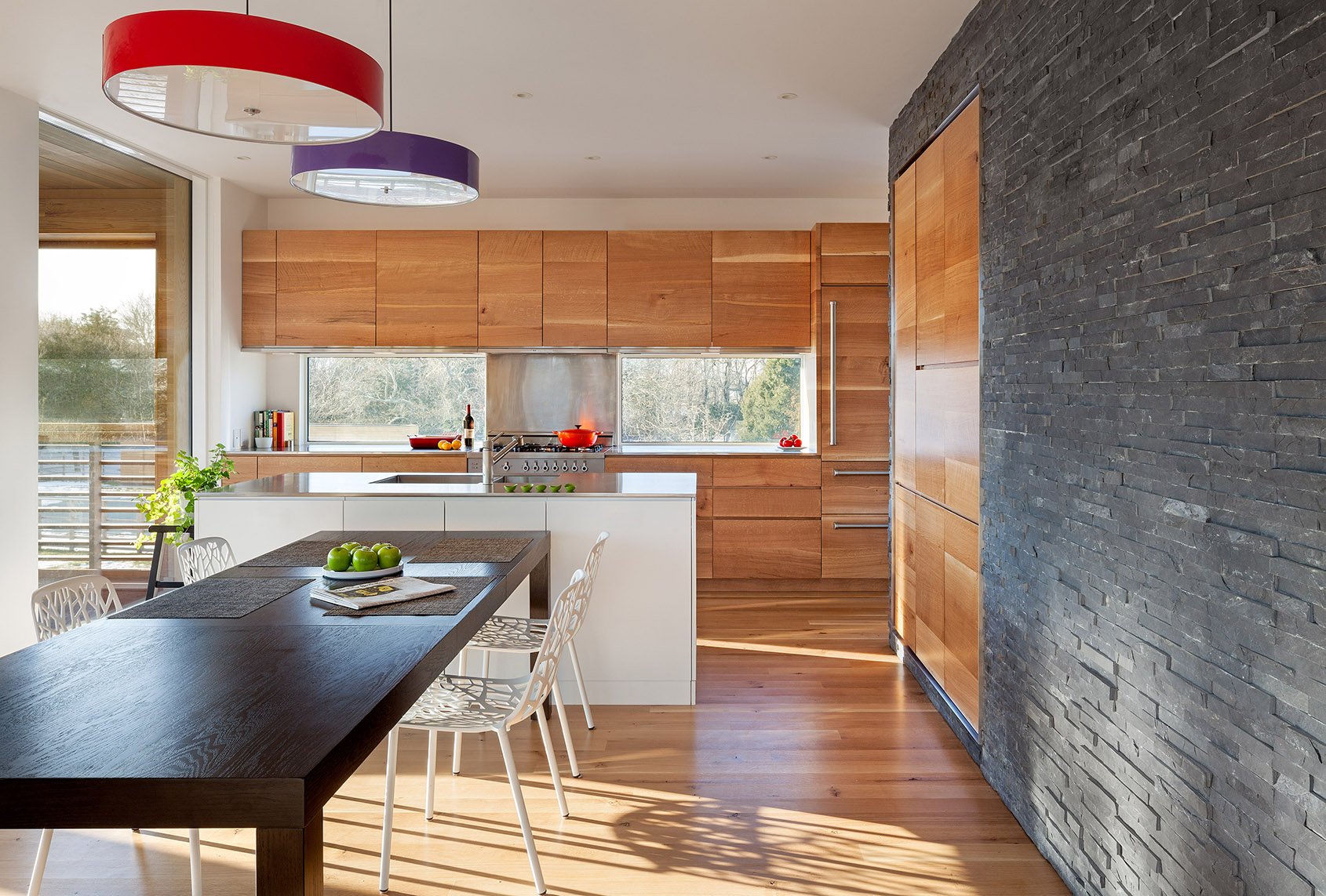 Modern kitchen with wooden cabinets, a white island, a dining table with green apples, and black textured wall.