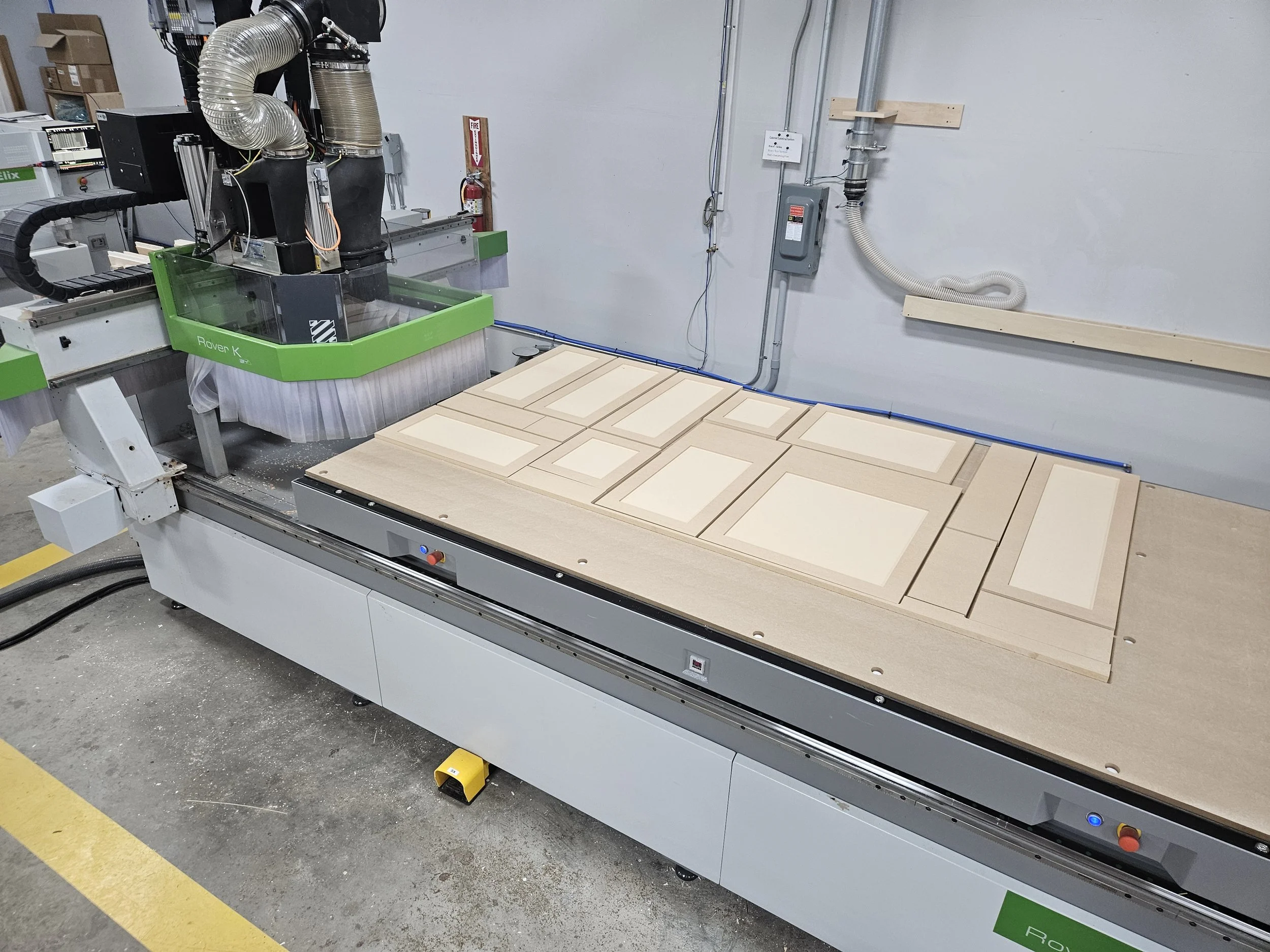 CNC machine with multiple wooden and foam pieces on the bed, in a manufacturing workshop.