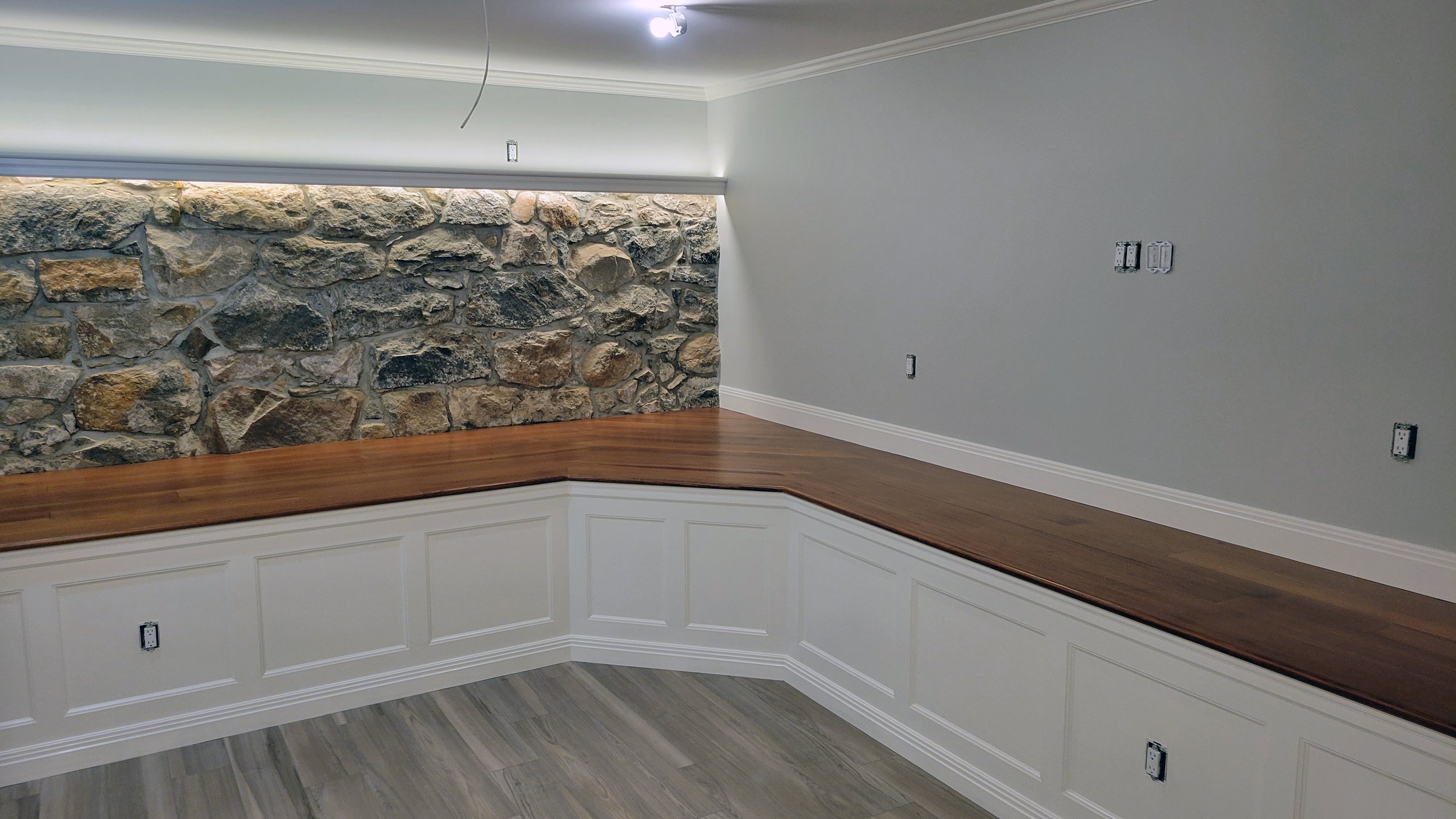 Interior of a room with a stone accent wall, white wainscoting, and a wooden floor with a built-in bench or platform.