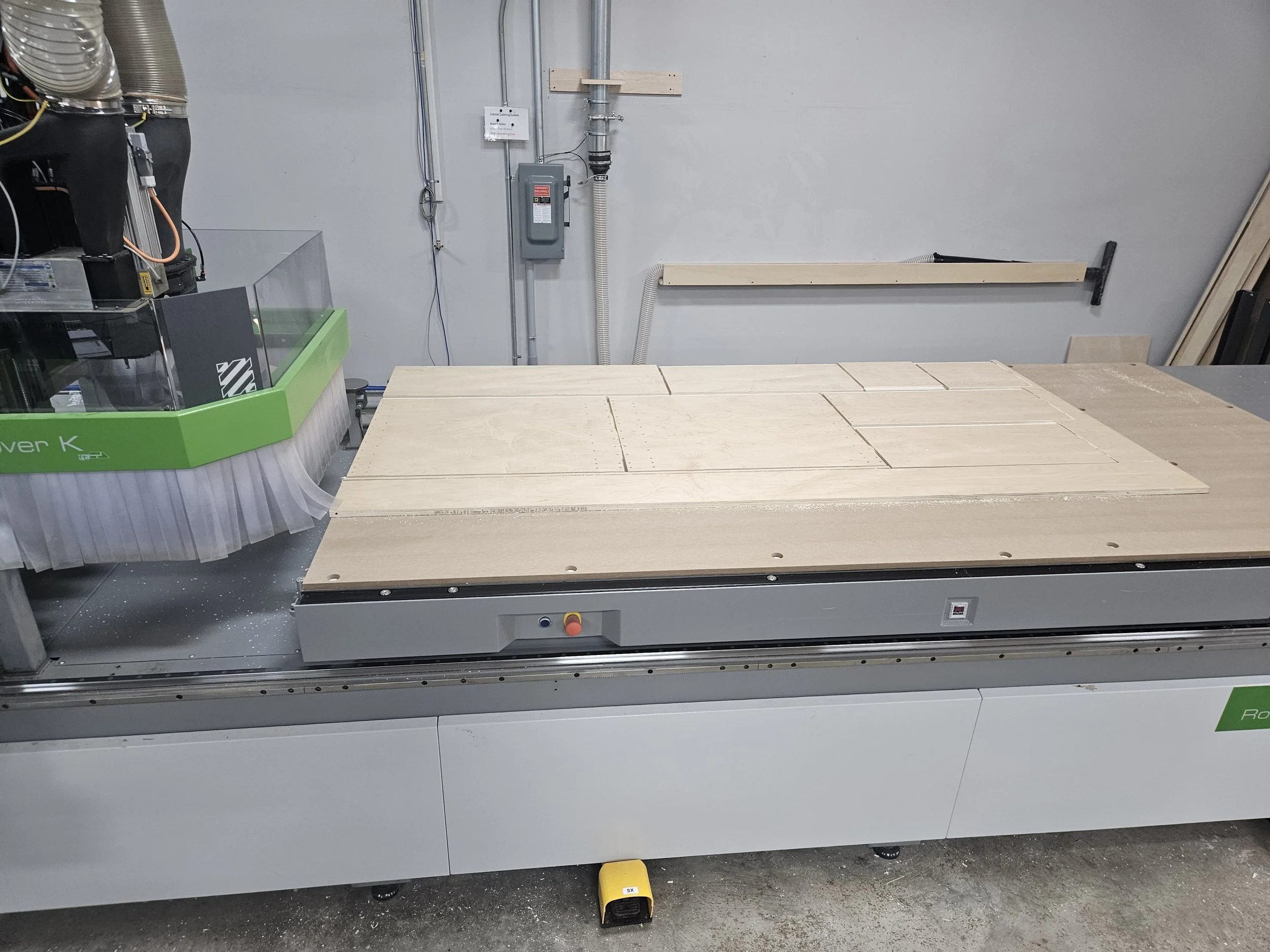 A woodworking CNC machine cutting rectangular wooden panels in a workshop.