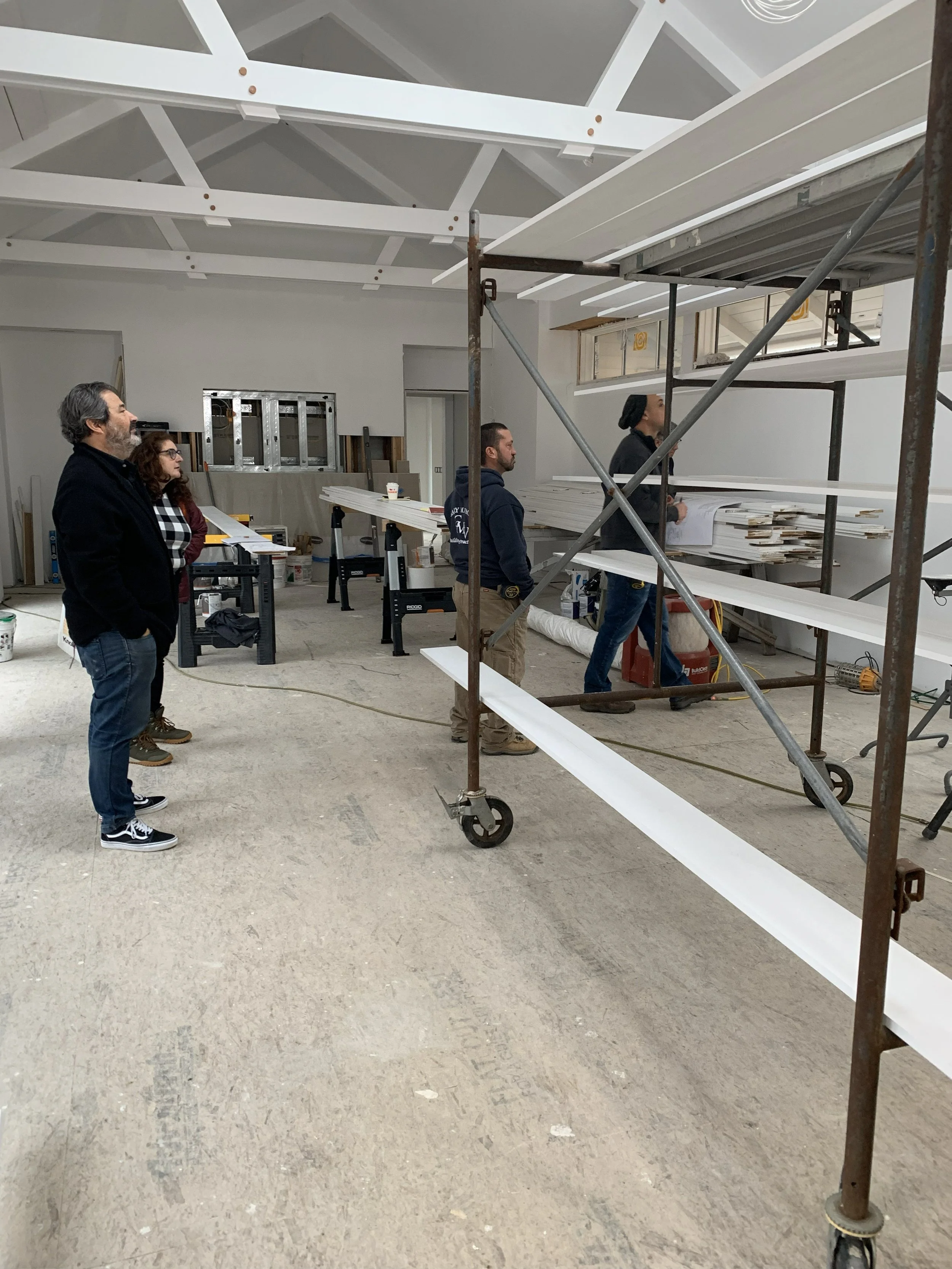 Four people inside a construction site looking at it. The space is under renovation with exposed ceiling beams and construction materials on a scaffold.