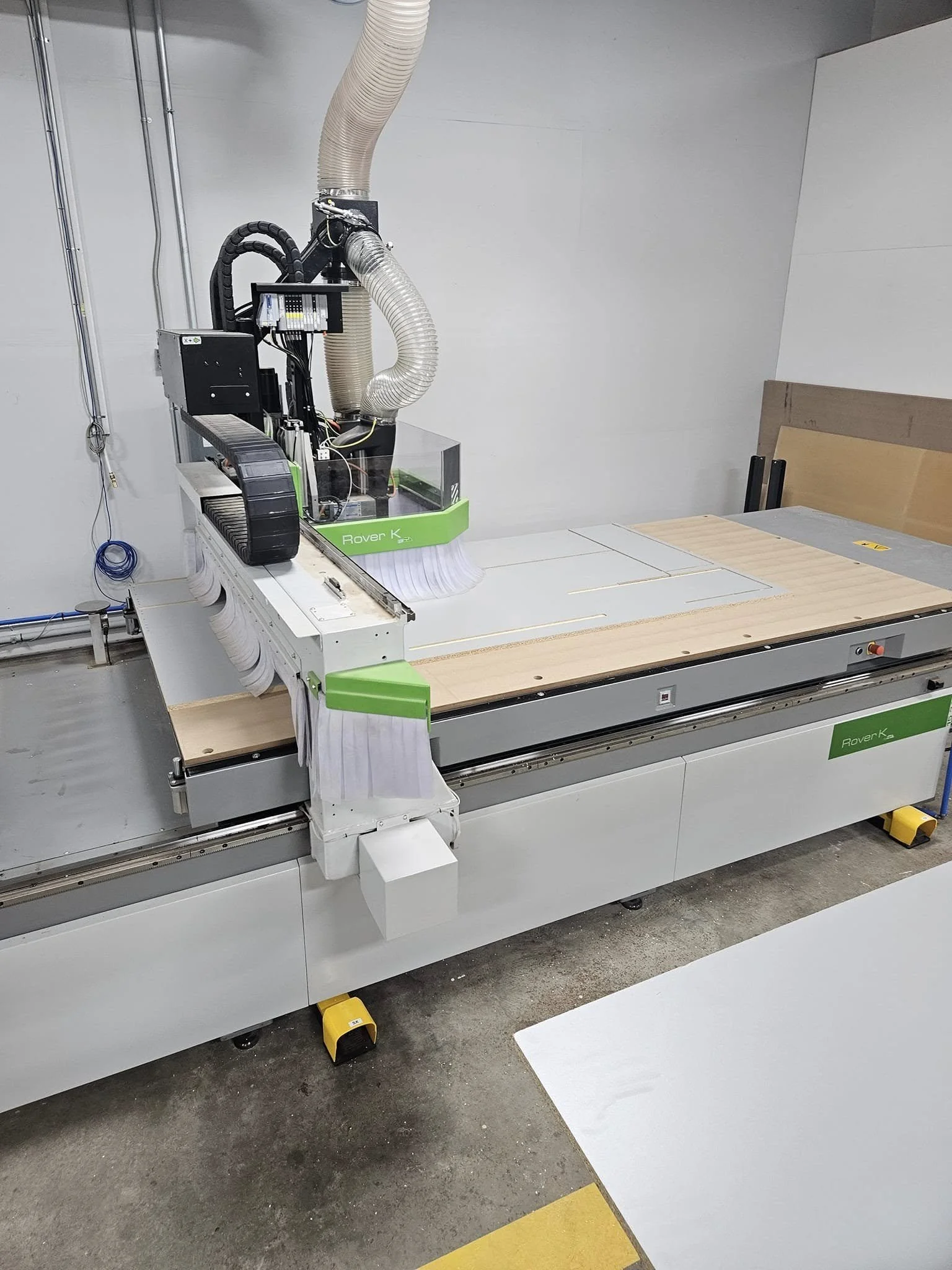 A large CNC machine in a workshop or factory setting, with vacuum hoses and a wooden work surface.