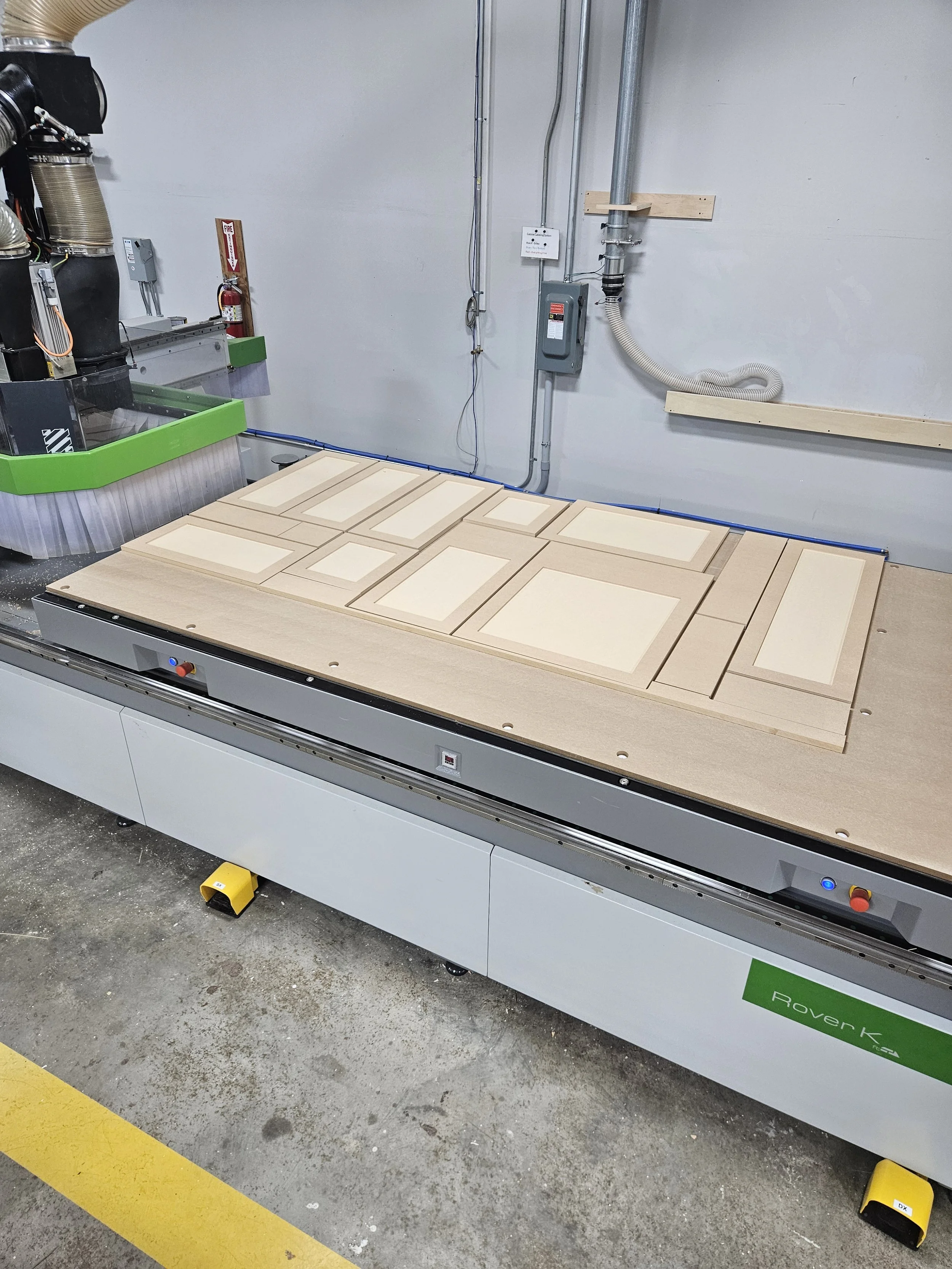 Wooden cabinet doors panels and frames on a CNC machine in a woodworking shop.