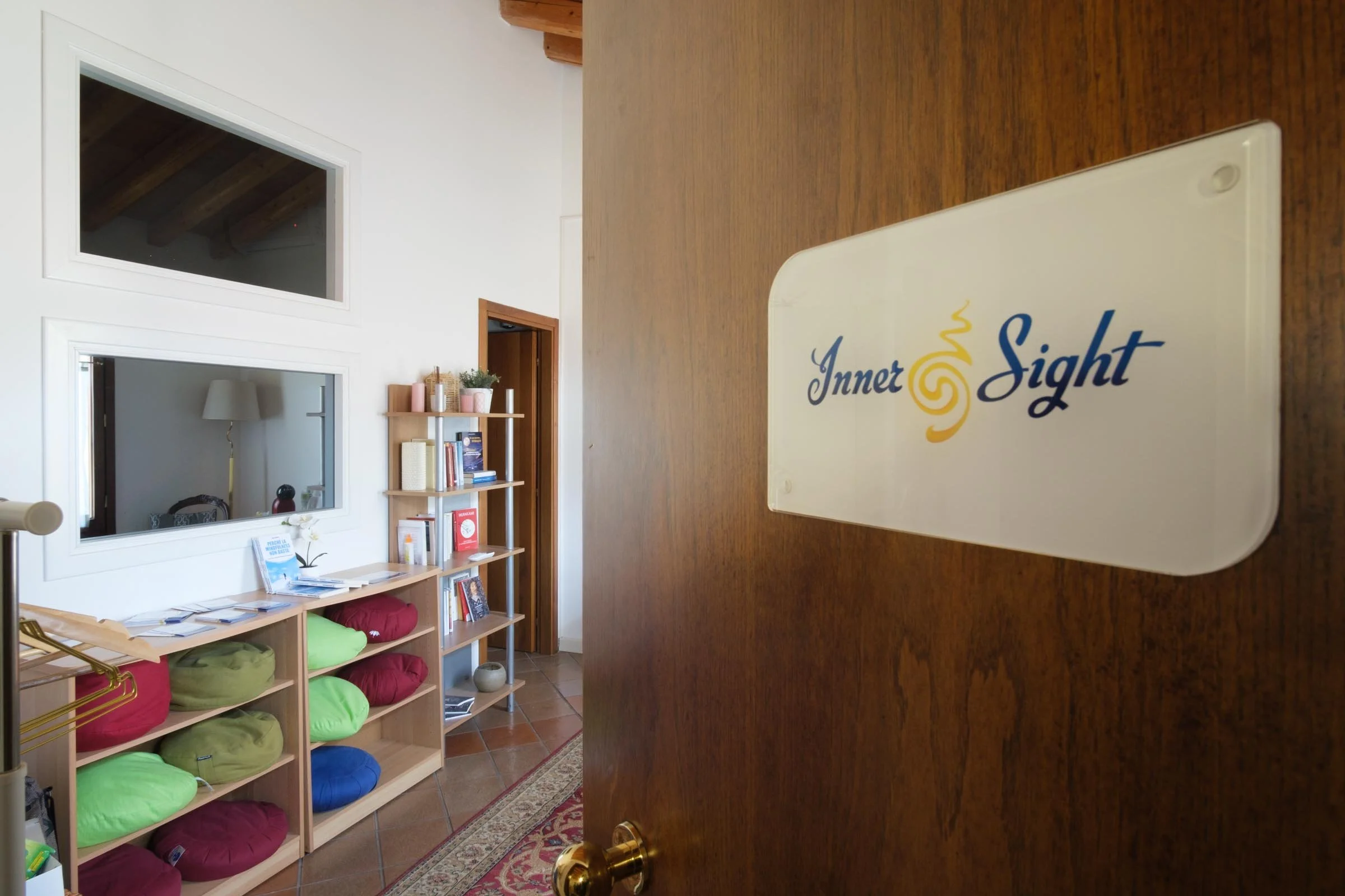 Interno di una sala con scaffali di libri e cuscini colorati, vista attraverso una porta di legno.