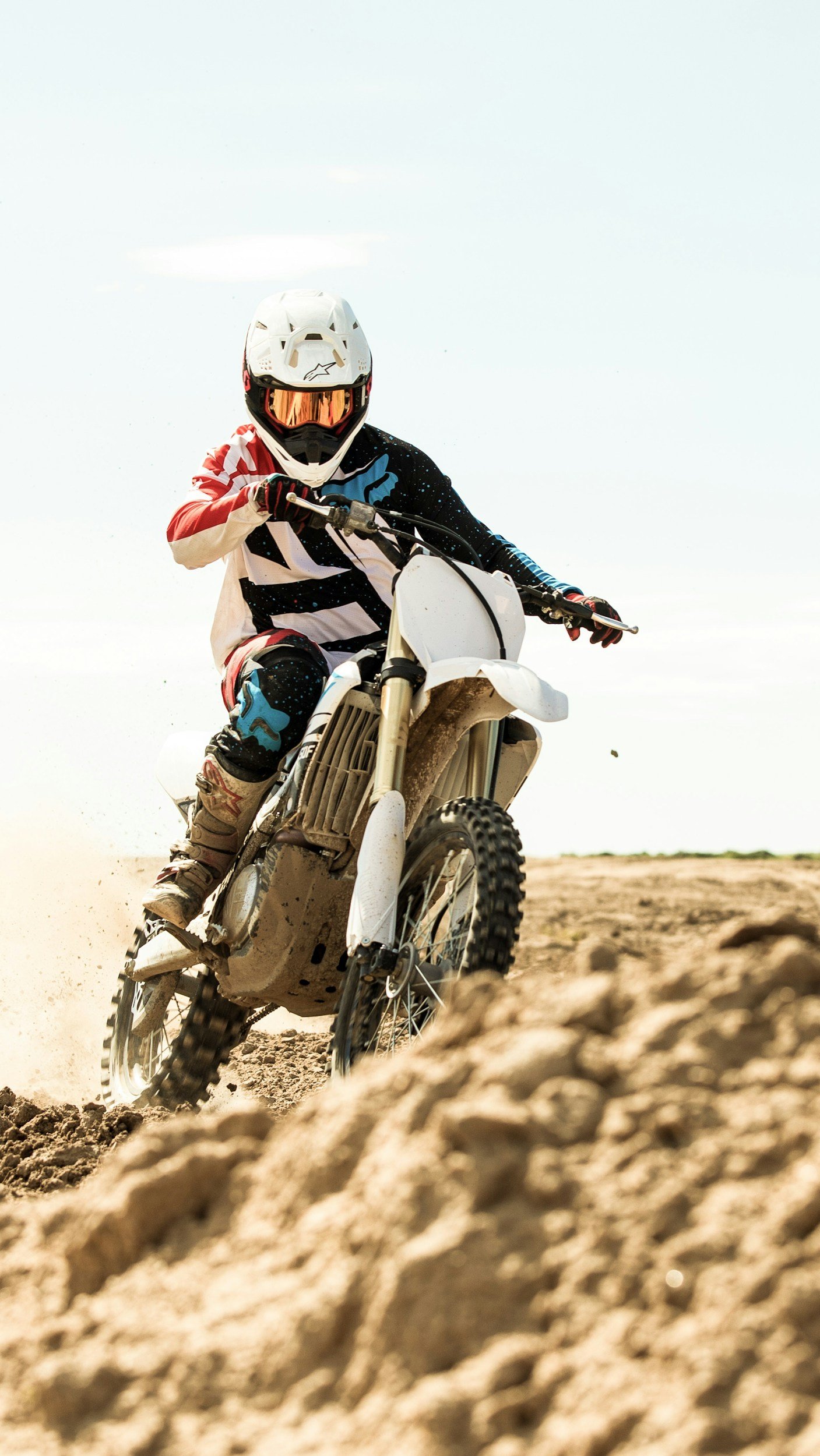 A motocross rider in full gear riding on a dirt track, with a view of the motorcycle and off-road terrain.