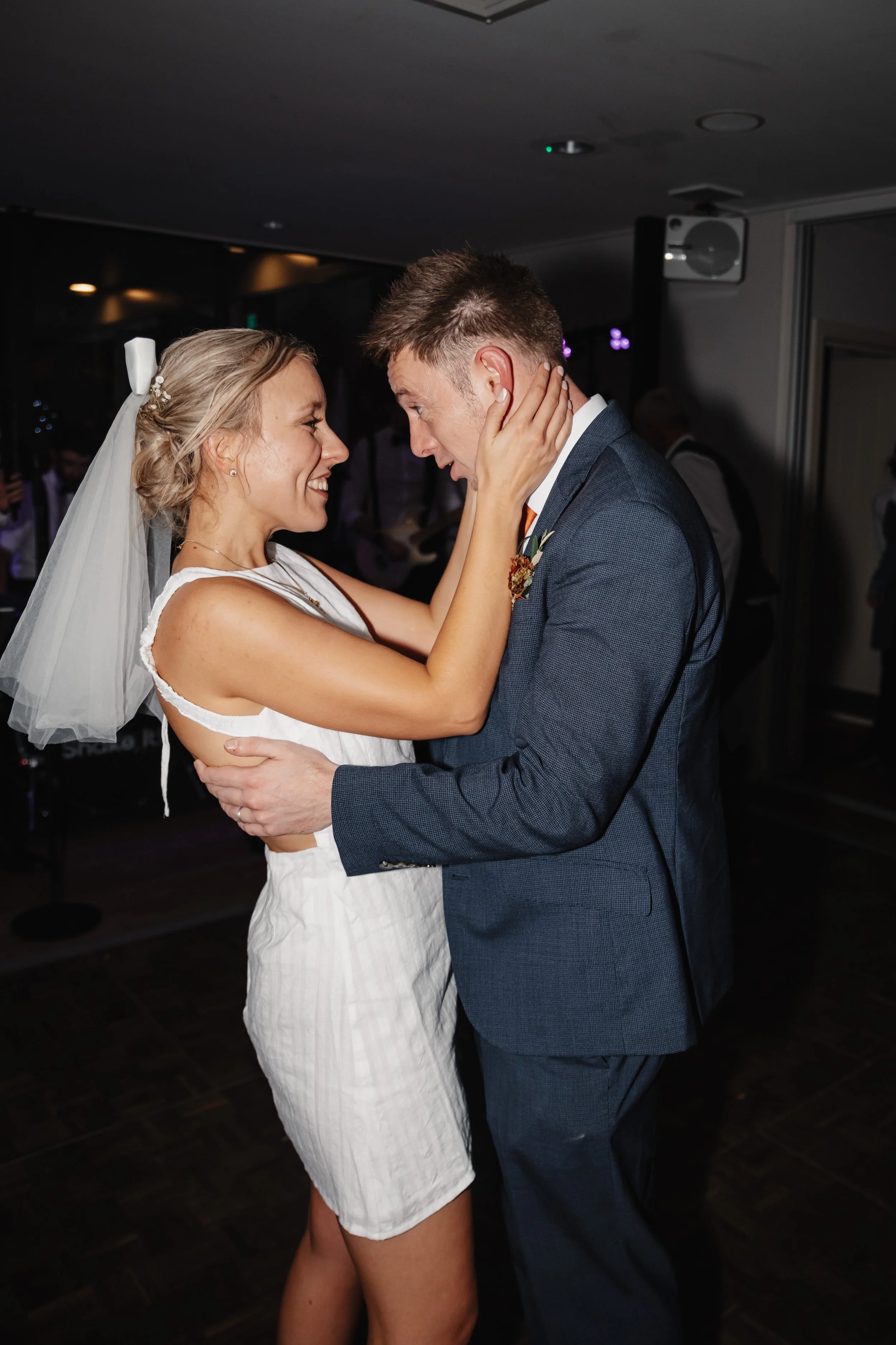 A bride and groom share a dance during their wedding reception, smiling at each other.