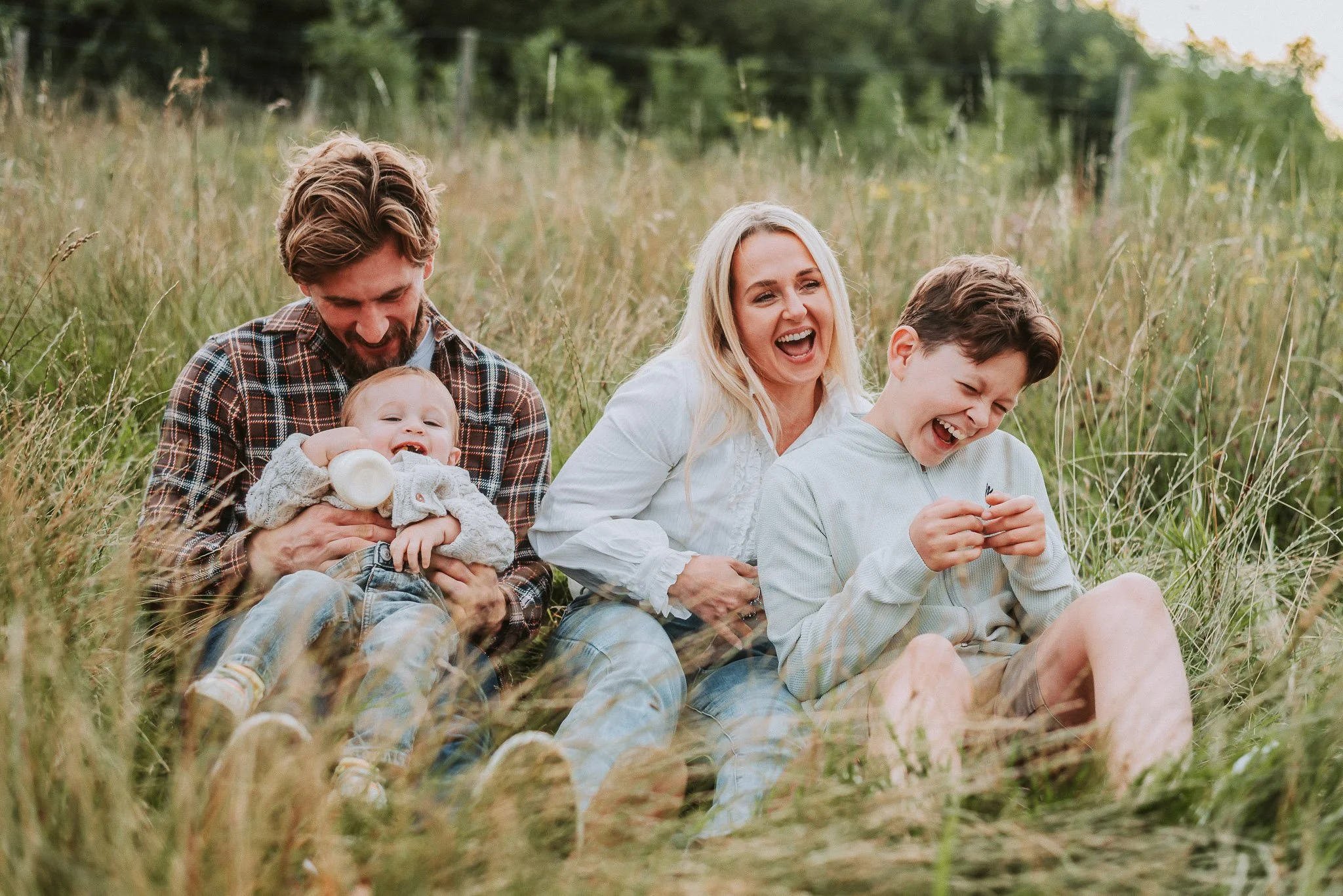 A happy family of four sitting in a grassy field, laughing and enjoying their time together.