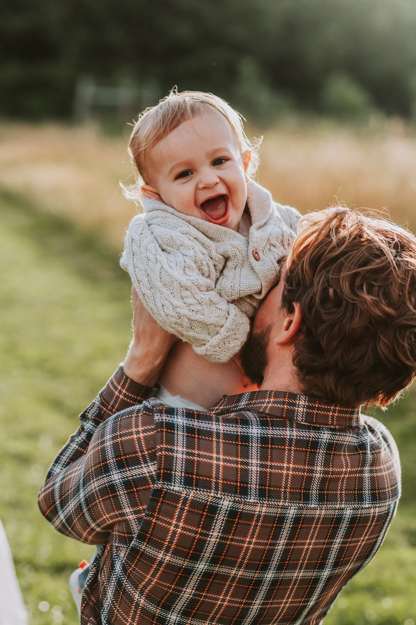 A man holding a smiling young child outdoors in a grassy area at sunset.