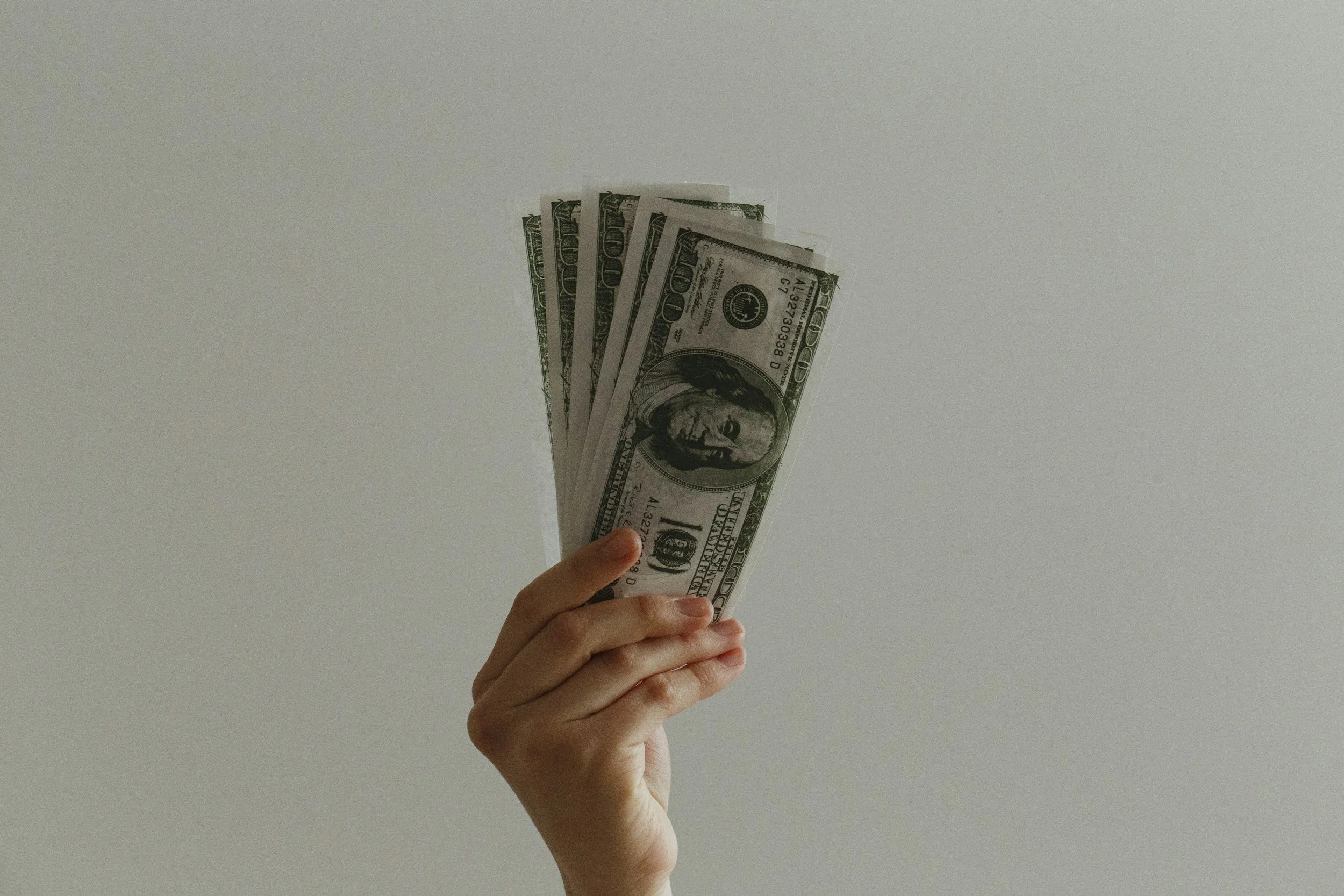 A hand holding several hundred-dollar bills against a plain white background.