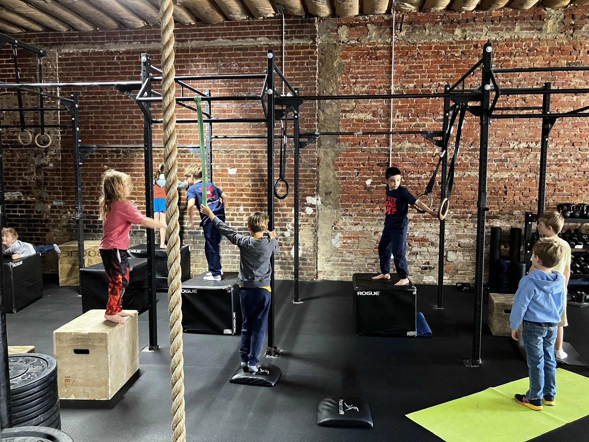 Children practicing and playing with gymnastics and climbing equipment in a gym.